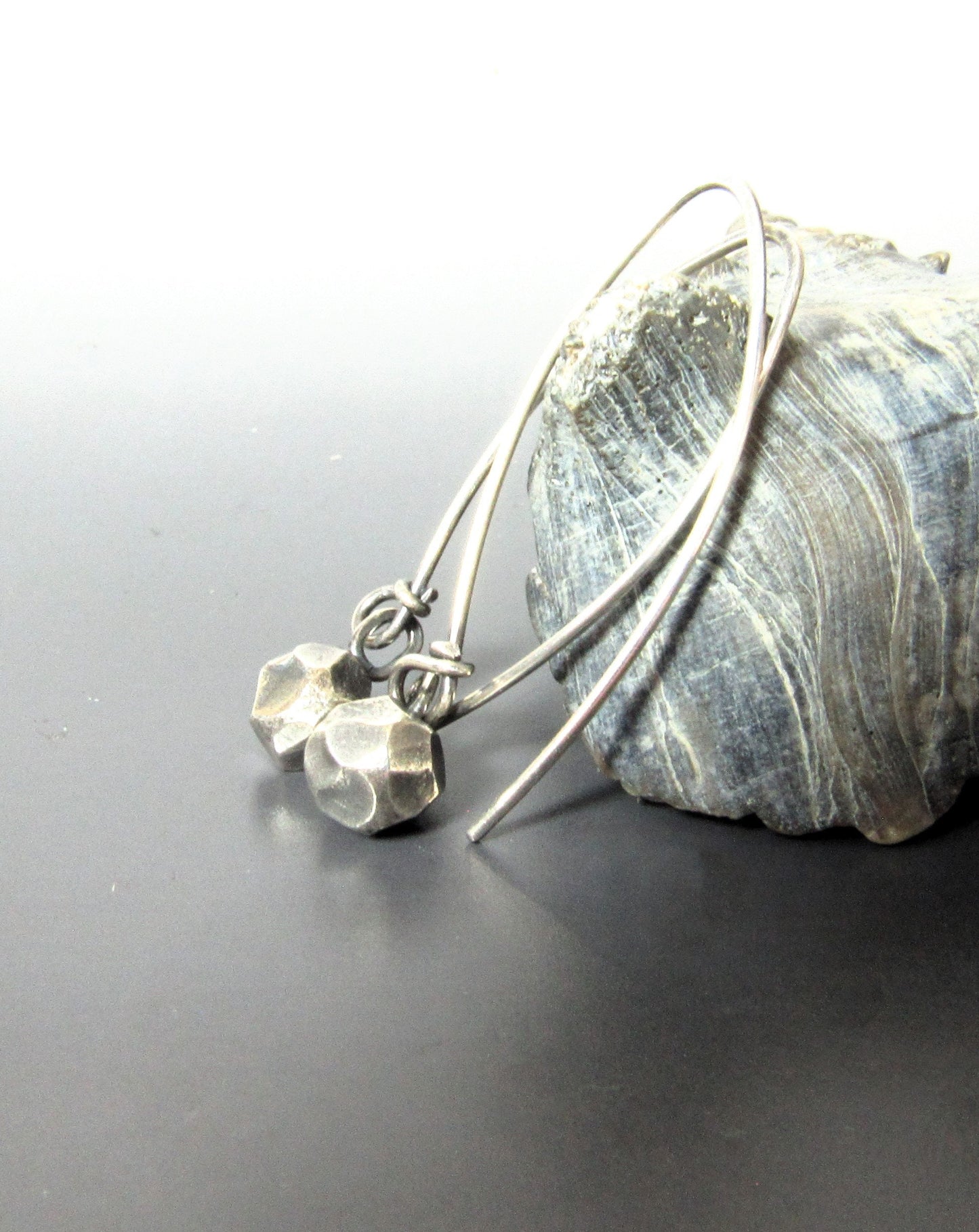Faceted SS nugget earrings against shell on dark background.