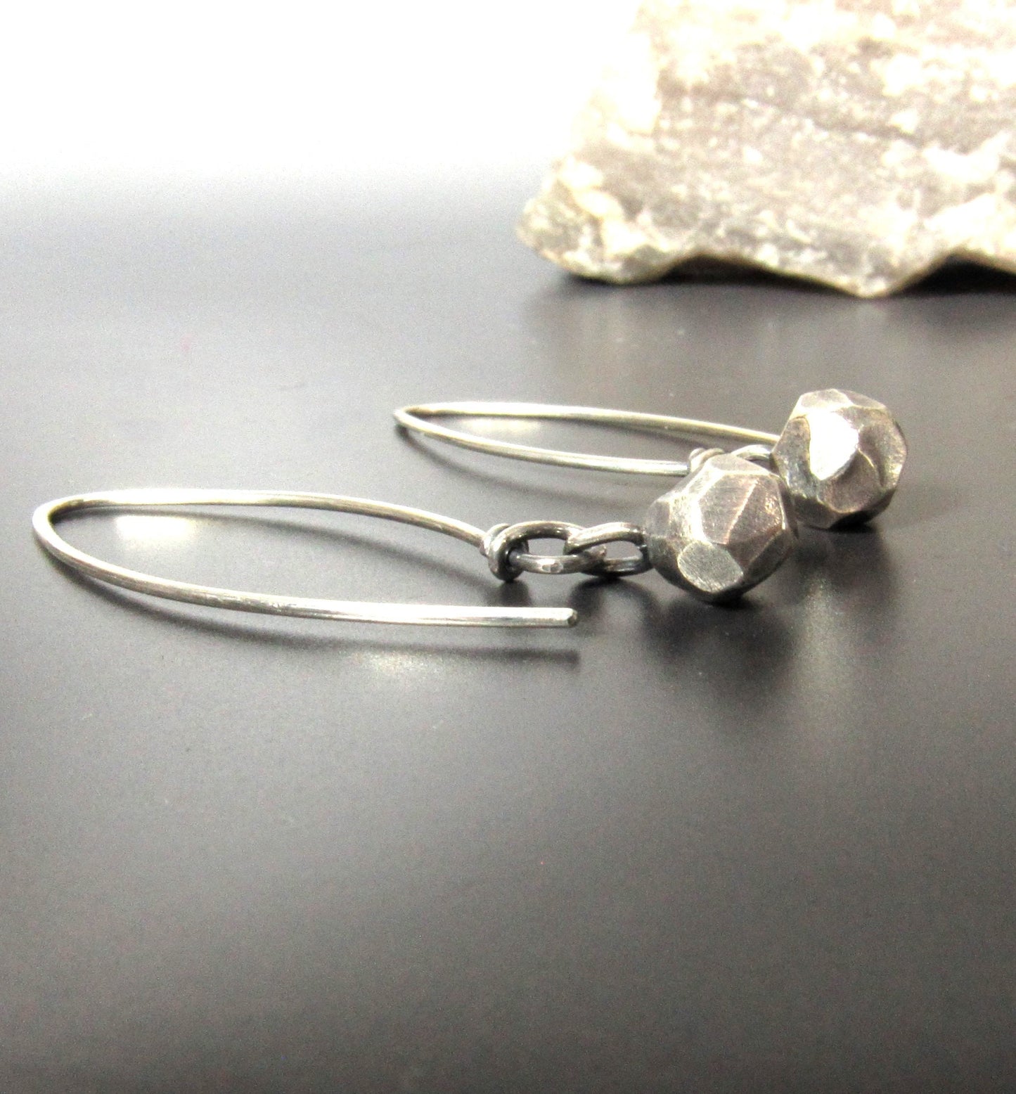 Hand faceted argentium SS nugget earrings on long ear wires with rock on dark background.