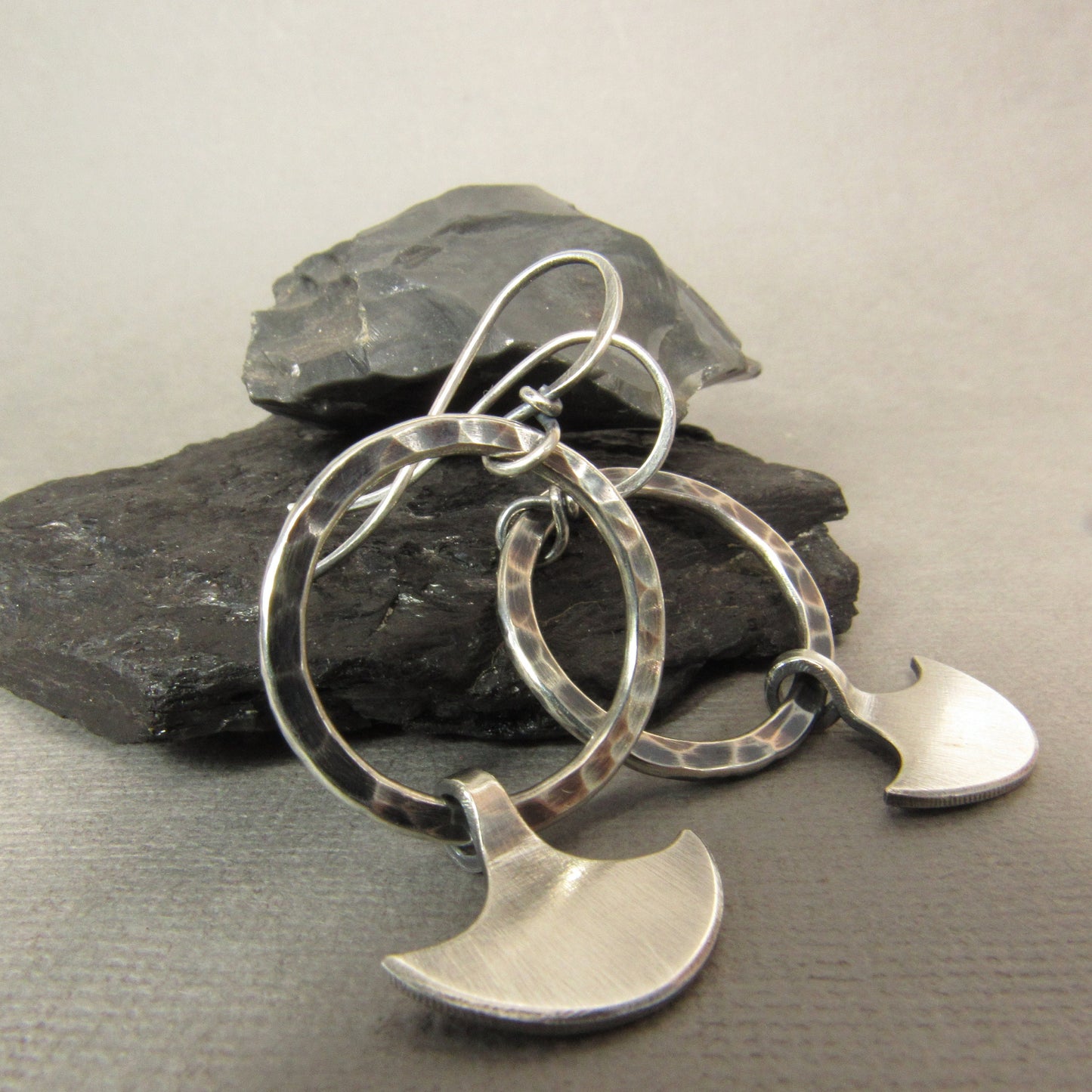 Axe hoop dangle earrings against black rock.