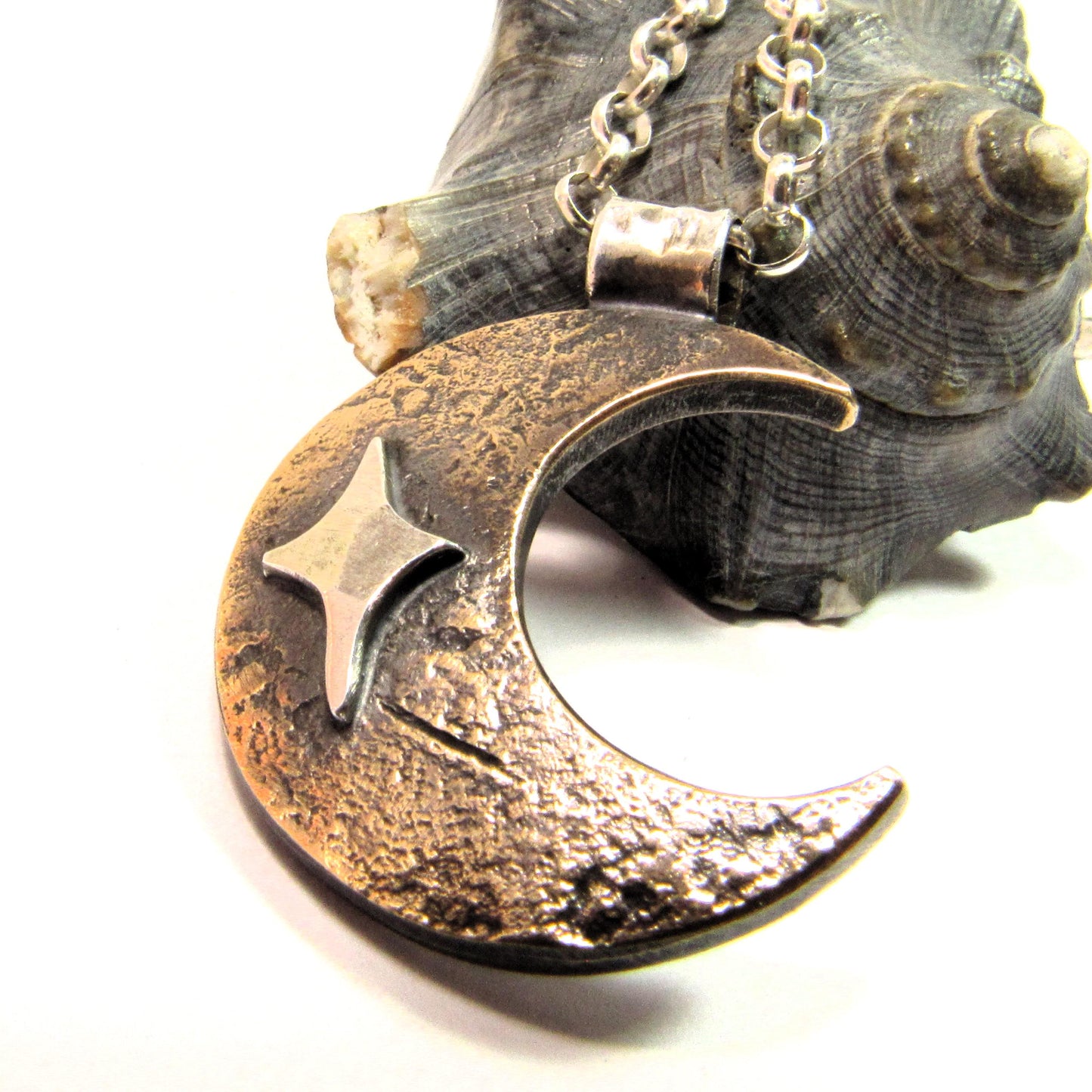 Mixed metal star and moon unisex pendant necklace on white background with sea shell.