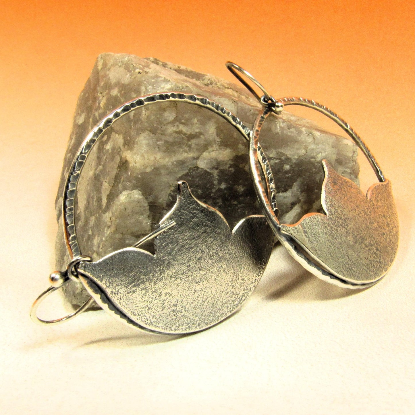 Large SS statement earrings with lotus shape on orange background against rock.