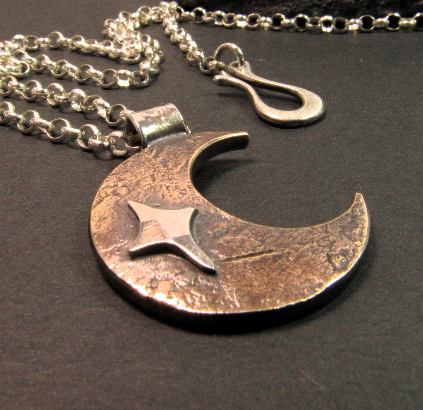 Rustic unisex crescent moon pendant necklace in copper and silver on dark background.
