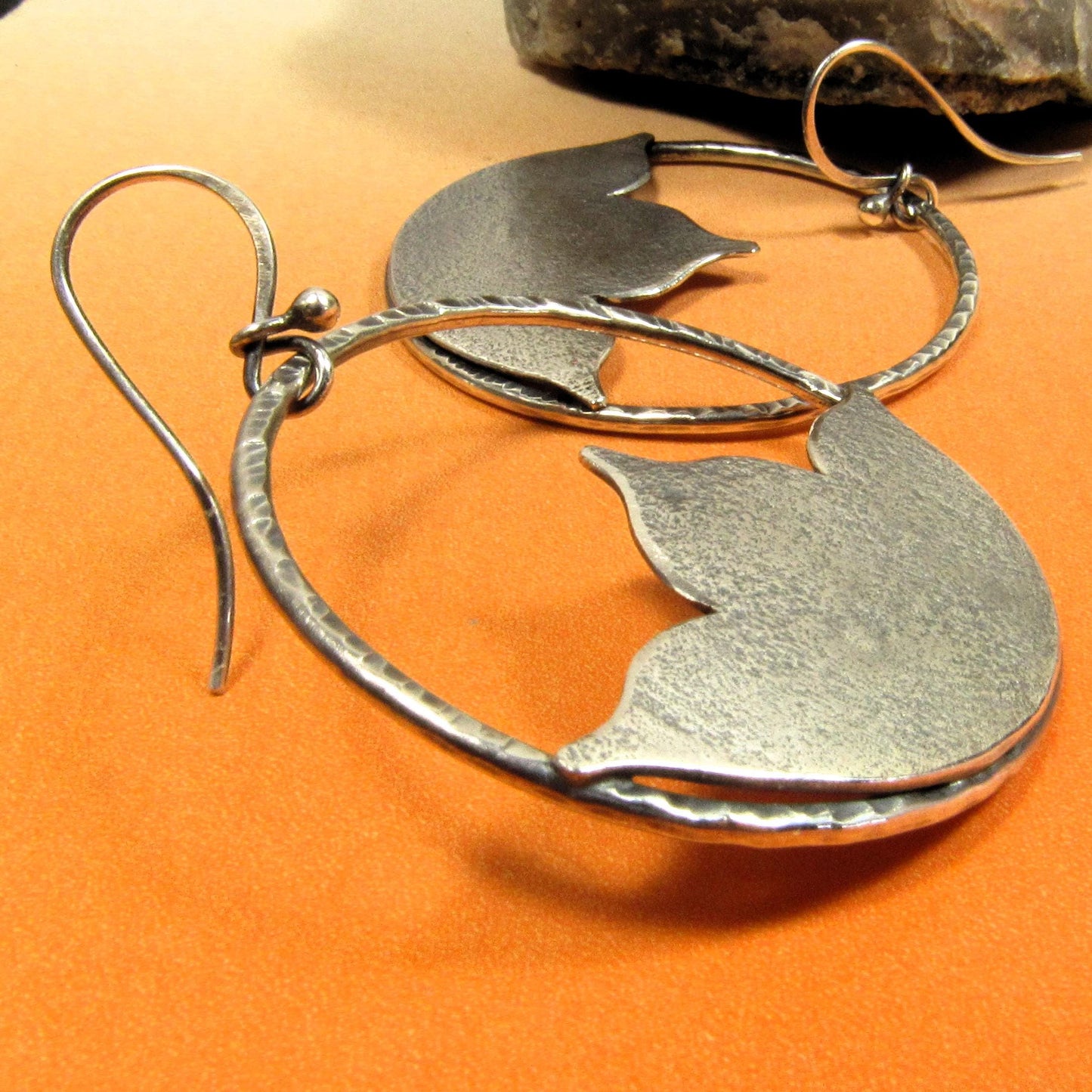 Side view large lotus earrings in argentium silver on orange background.