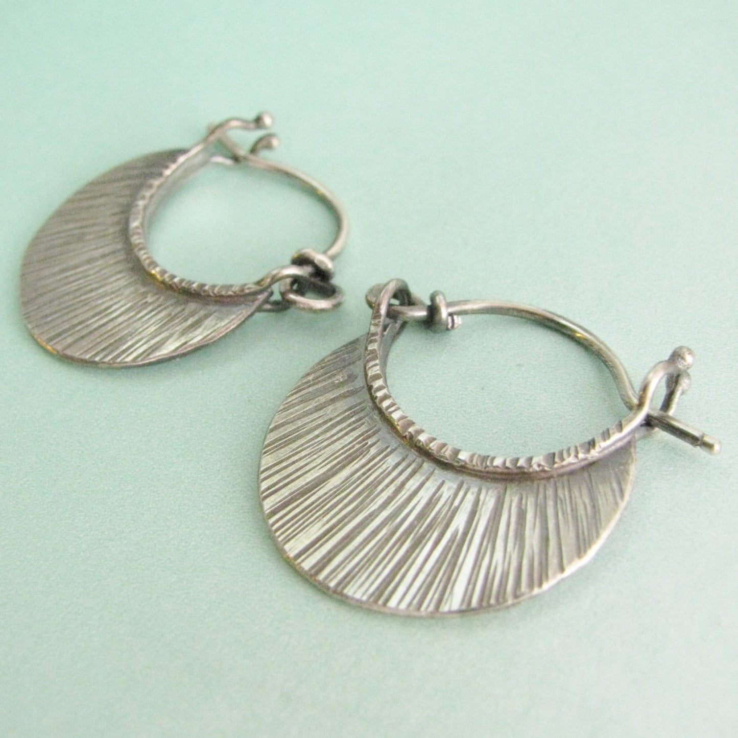 Hoop earrings in sterling silver, small modern style on blue background.