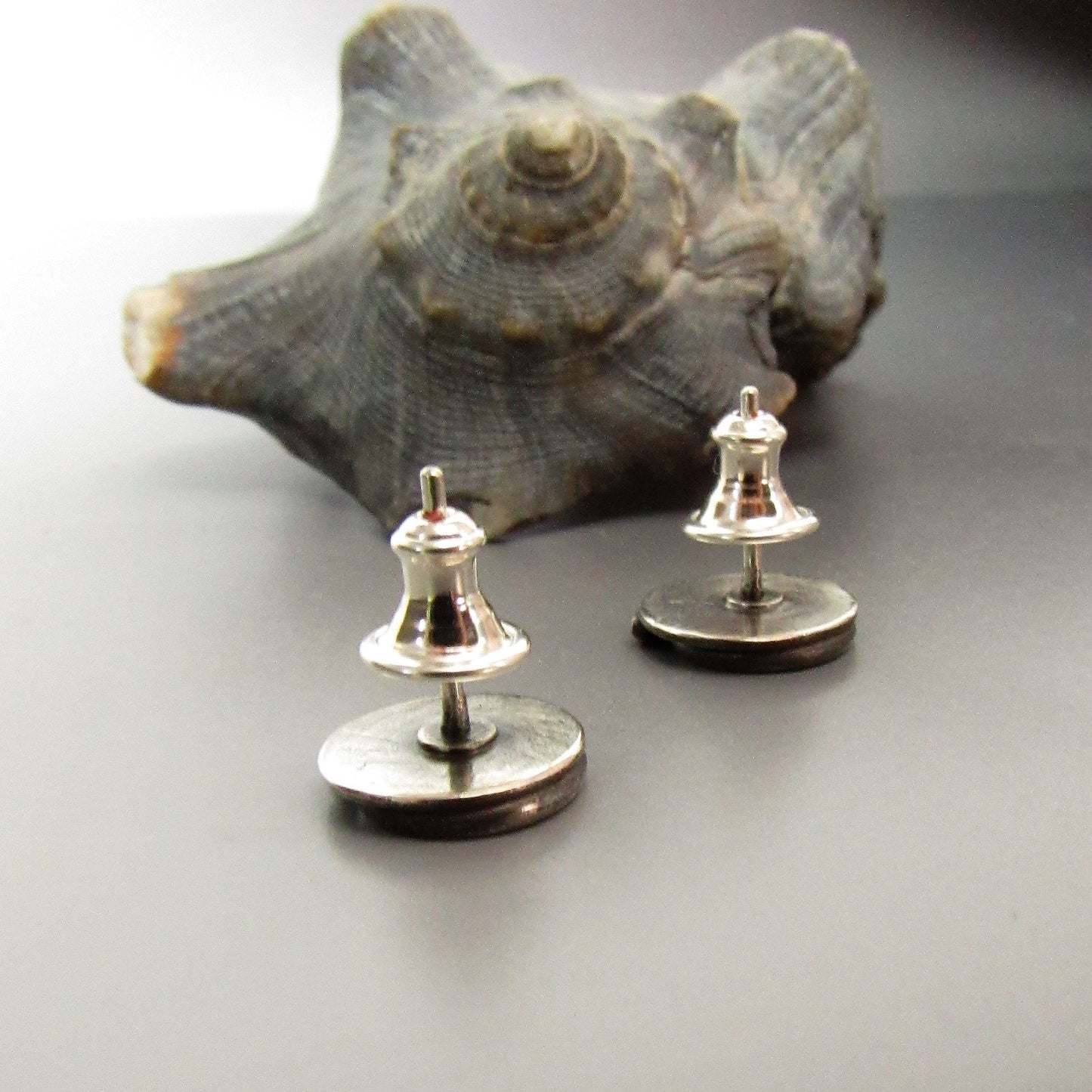 Back of SS spiral earrings with bullet clutches on a reflective surface with a large shell in the background.