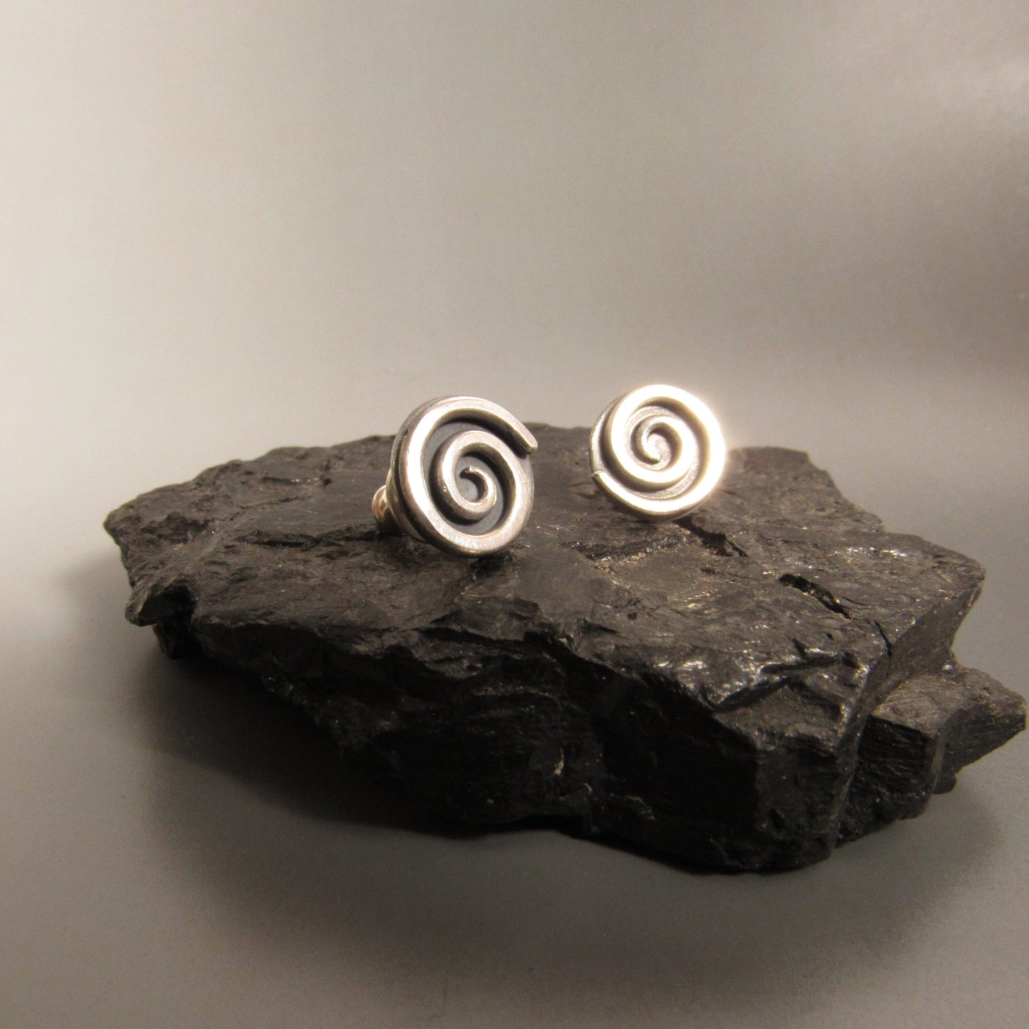 Silver spiral post back earrings on a dark stone surface