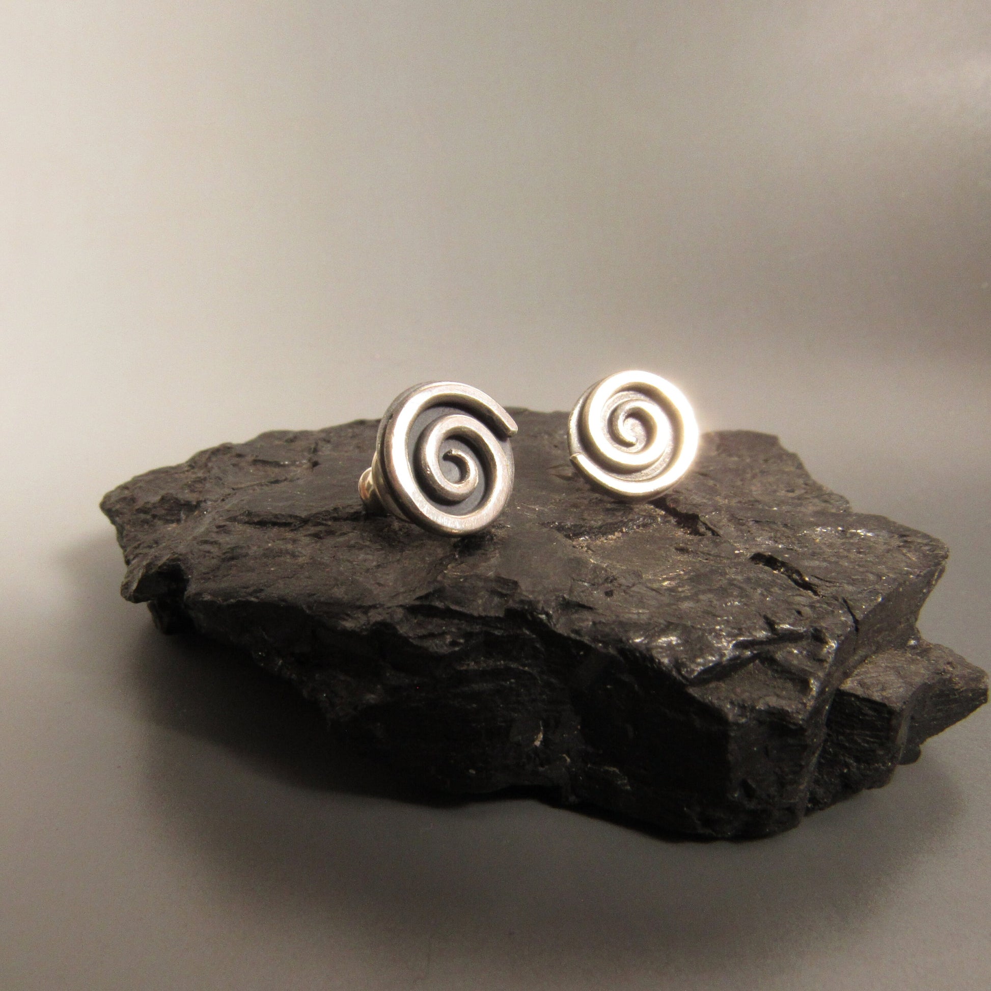 Silver spiral post back earrings on a dark stone surface