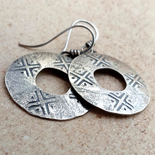 Handcrafted argentium SS coin style pair of silver earrings with geometric patterns on a beige background.