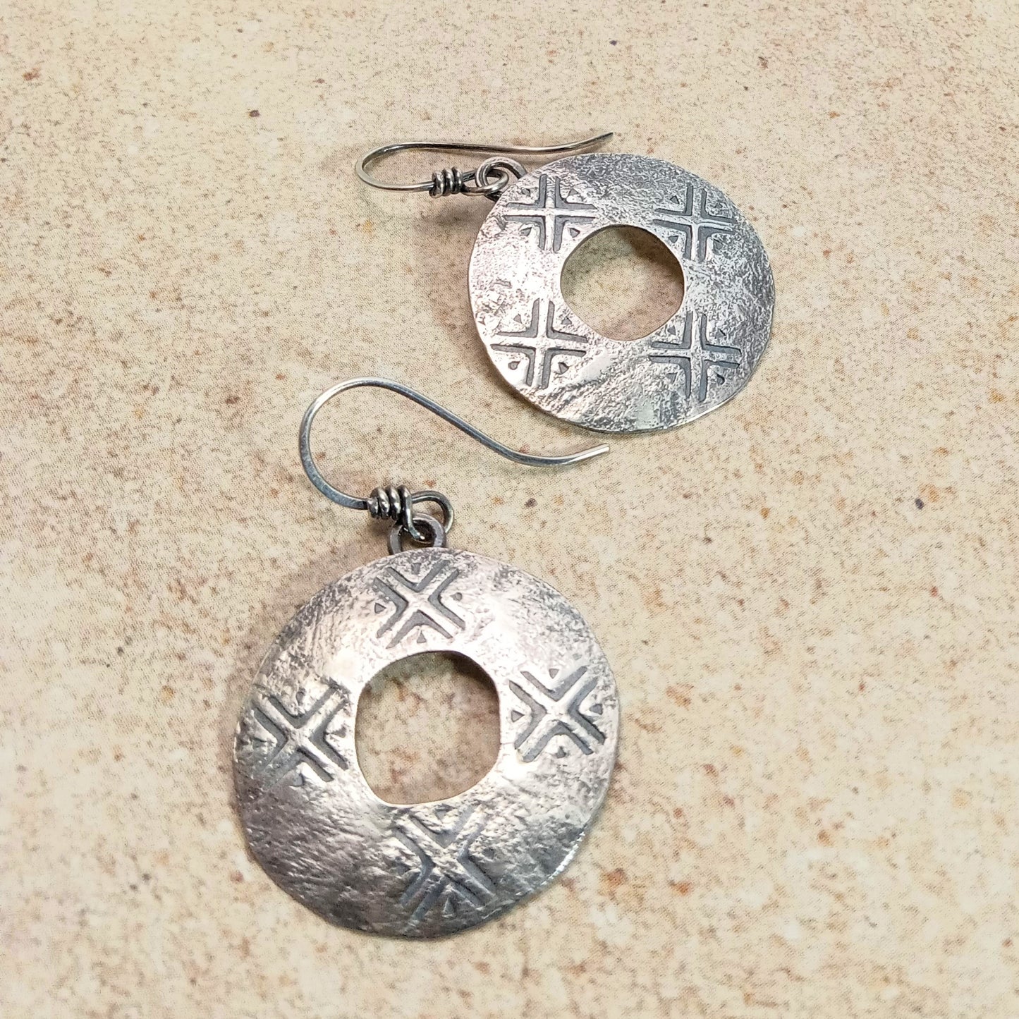 Pair of sterling silver round earrings with intricate stamped designs on a beige surface.