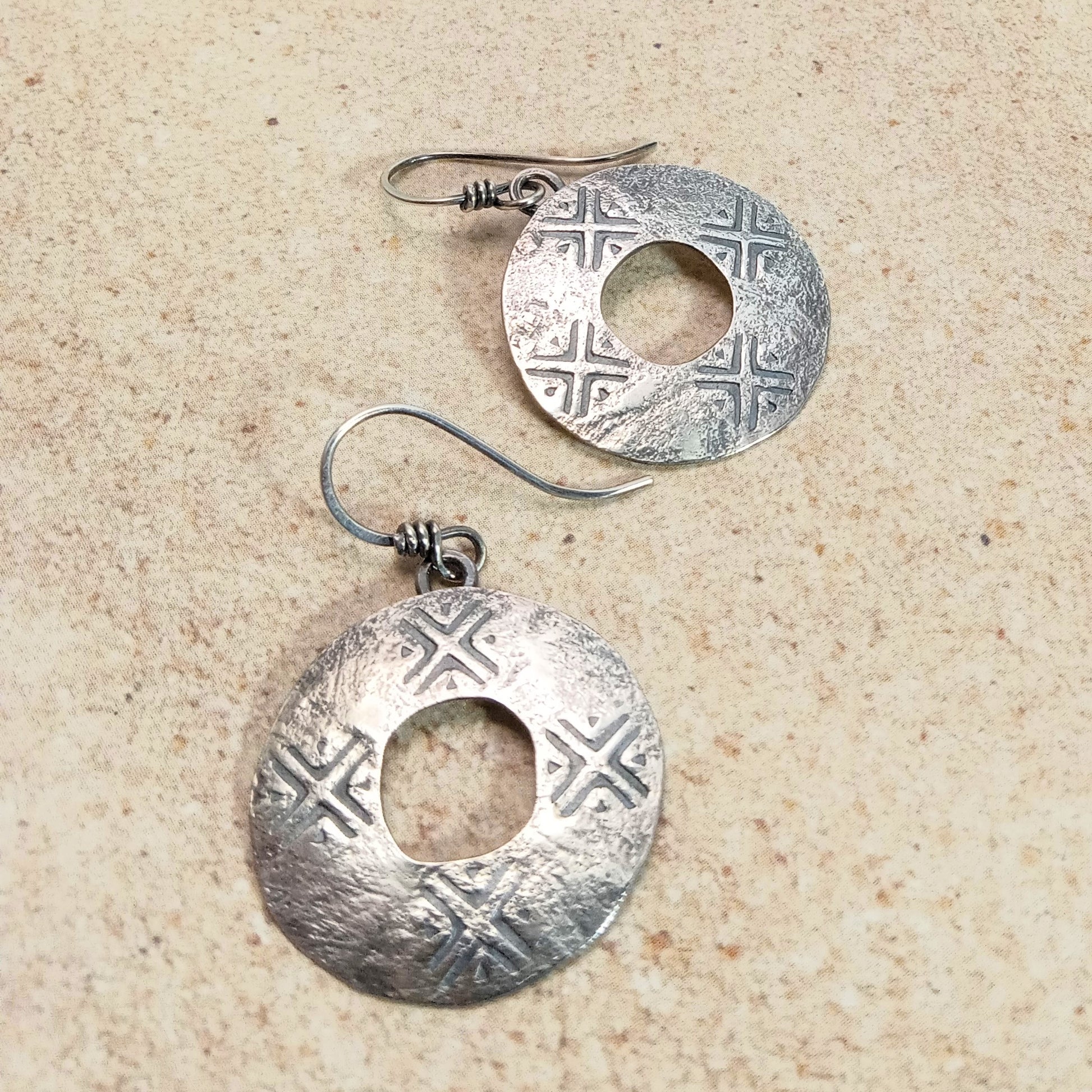 Pair of sterling silver round earrings with intricate stamped designs on a beige surface.