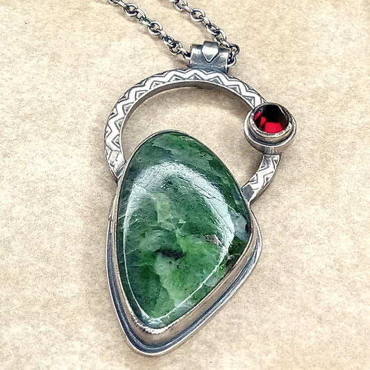 Argentium Silver pendant with green chrome diopside stone and red garnet gemstone on a beige background.