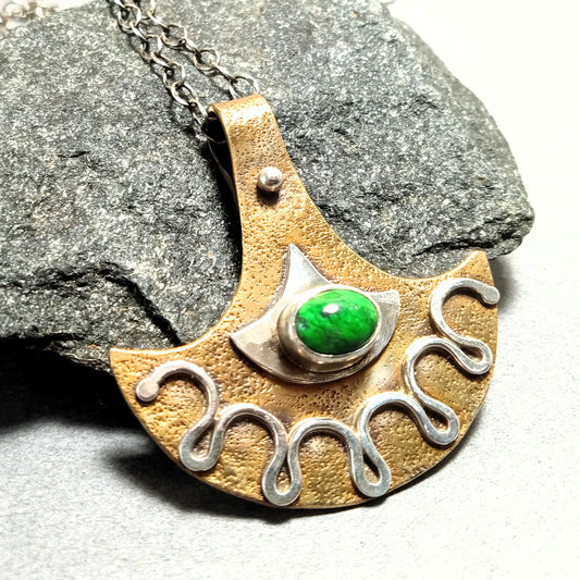Tribal-inspired bronze pendant with green Maw Sit Sit gemstone, sterling silver accents, and wave motif on rock background.