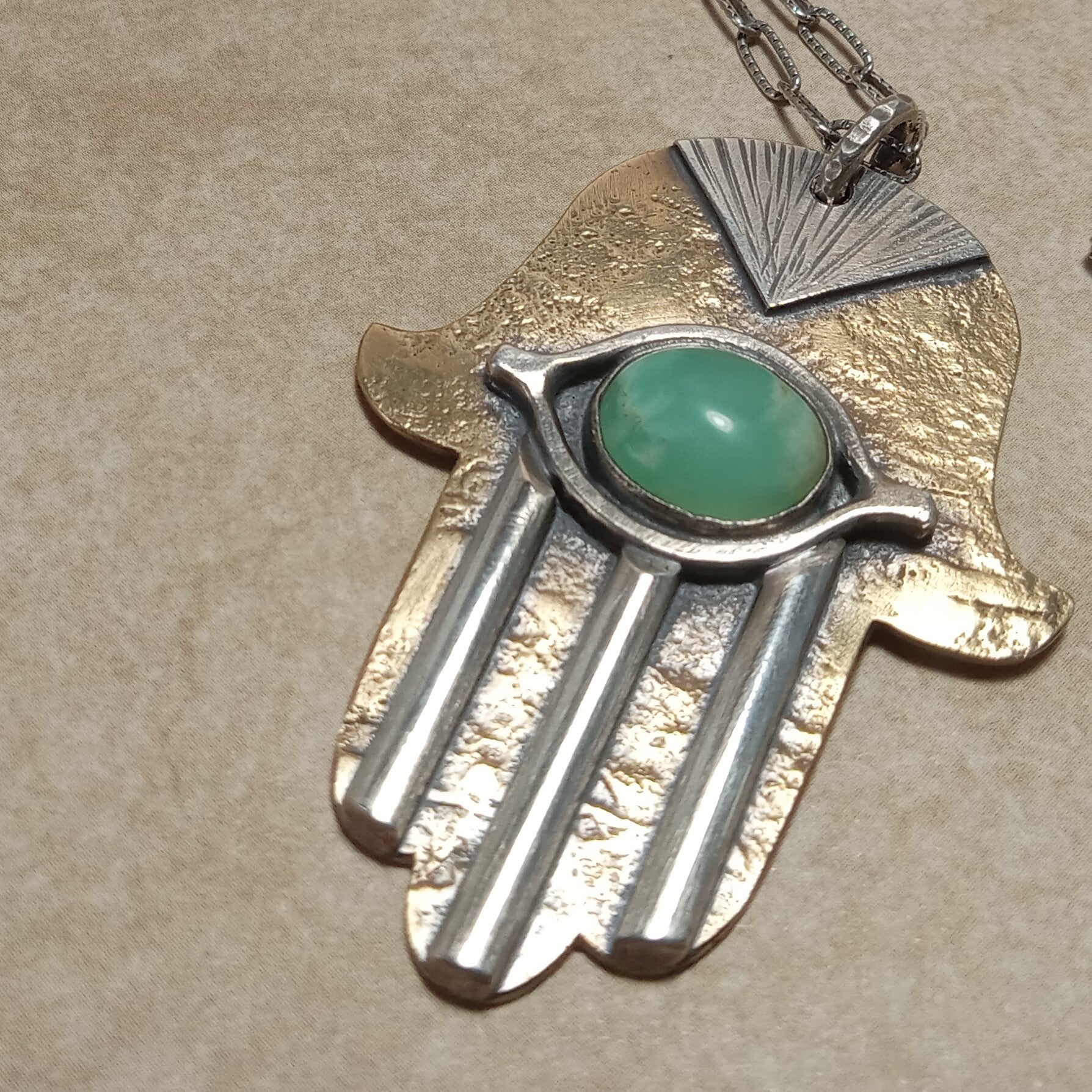 Angled shot of the Hamsa pendant showing depth, rustic texture, and oxidation finish of the bronze and silver.