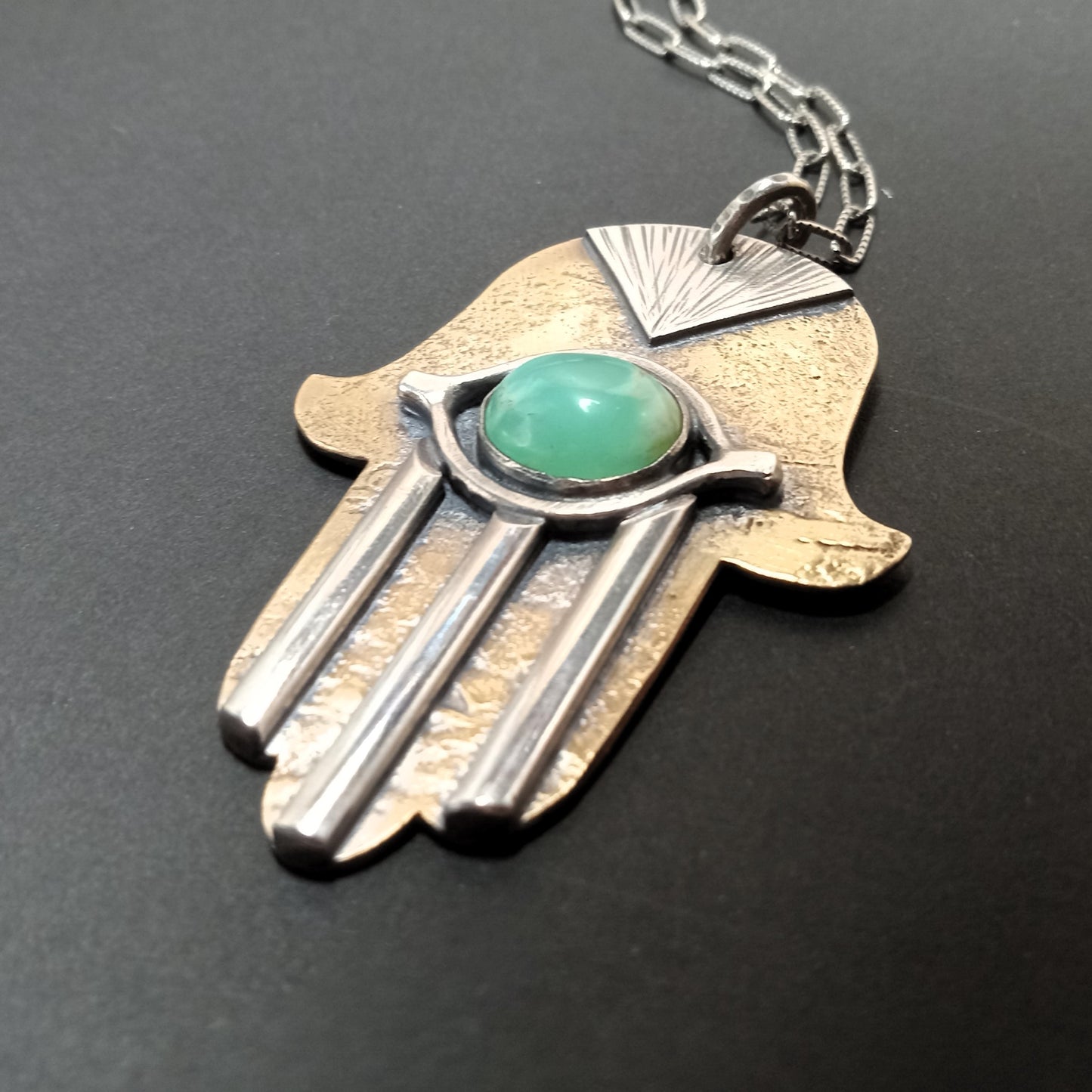 Hamsa hand pendant with a green gemstone on a black background