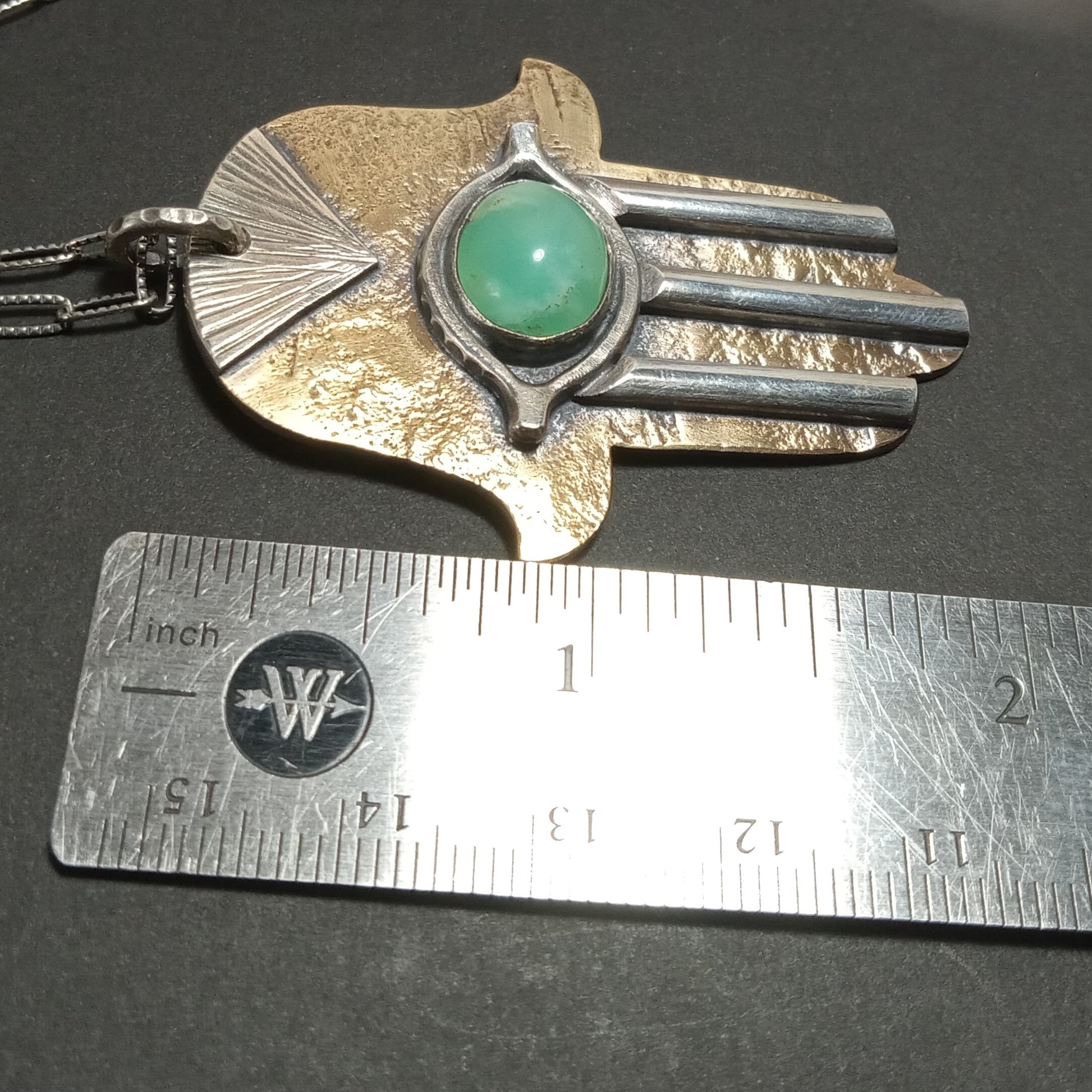 Handcrafted mixed metal Hamsa pendant by Mocahete next to ruler.
