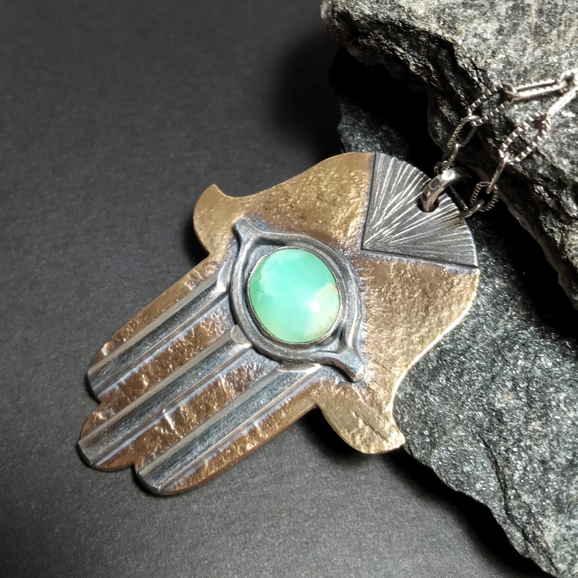 Chrysoprase Hamsa pendant necklace in bronze and sterling on dark rock background.