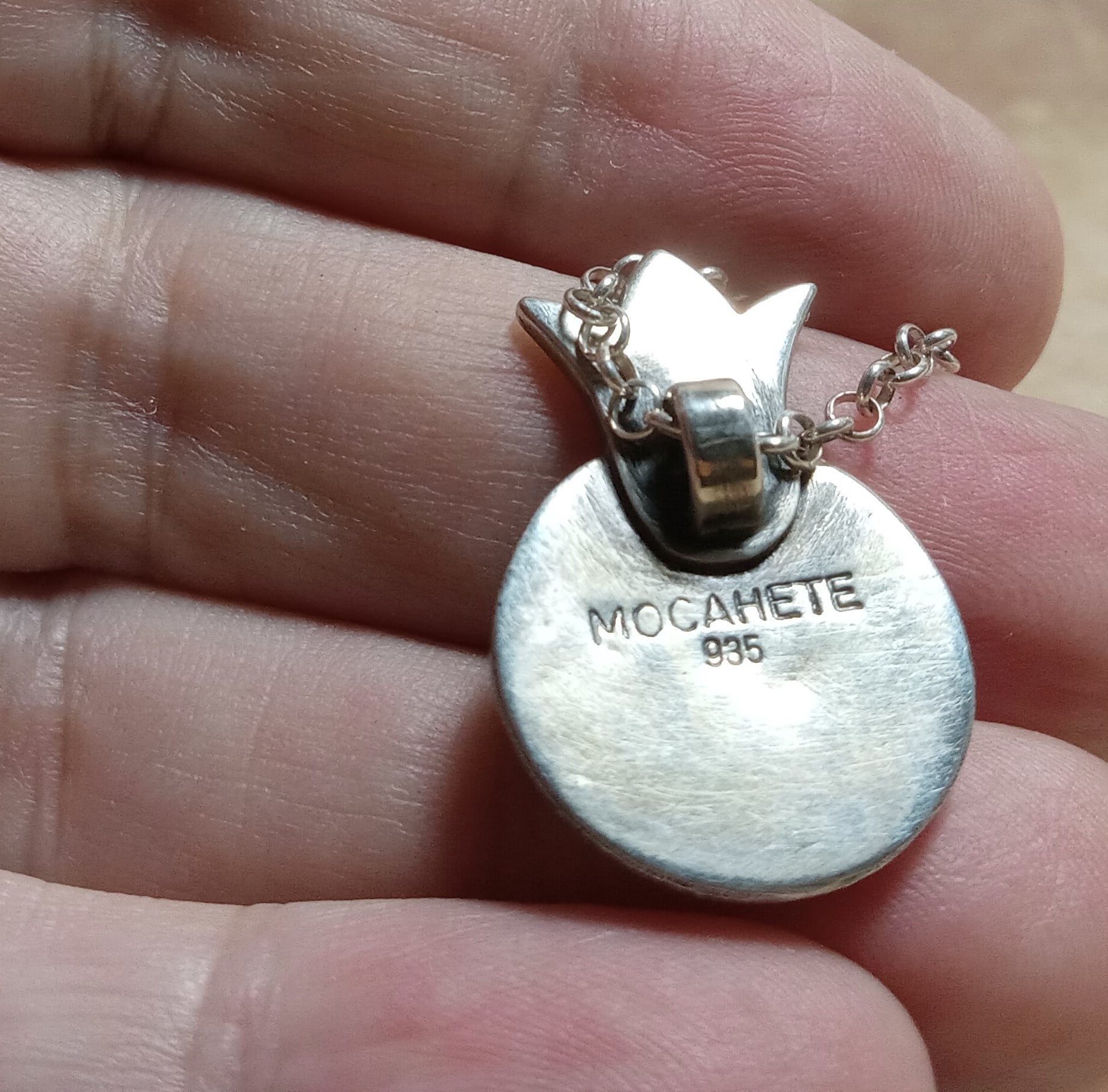 Argentium Silver pomegranate pendant showing makers mark  and 935 stamp held in a hand.