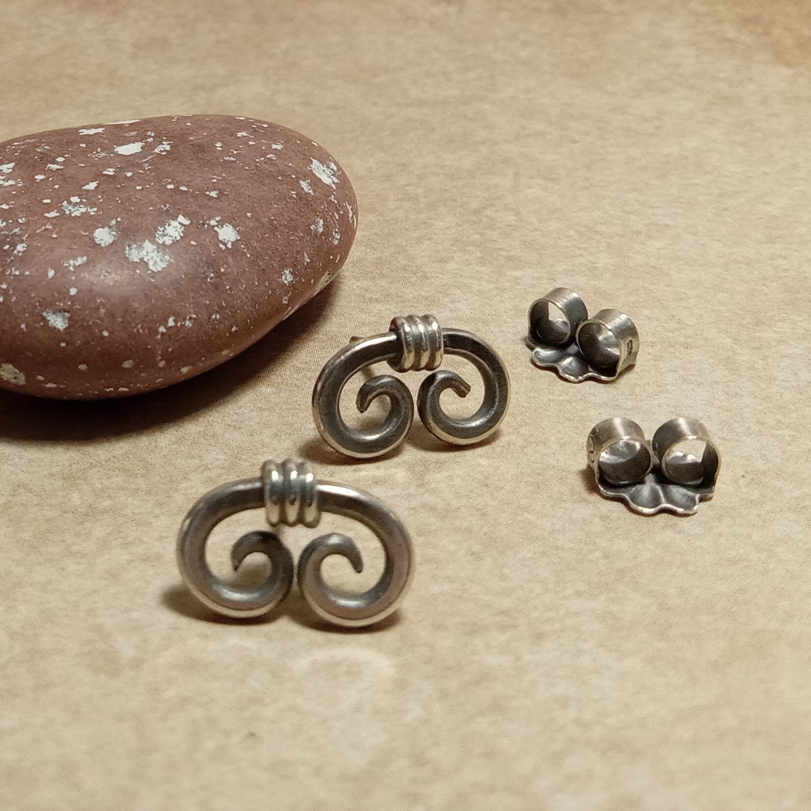 Front view of sterling silver spiral earrings with clutch backs on a beige surface with a stone.