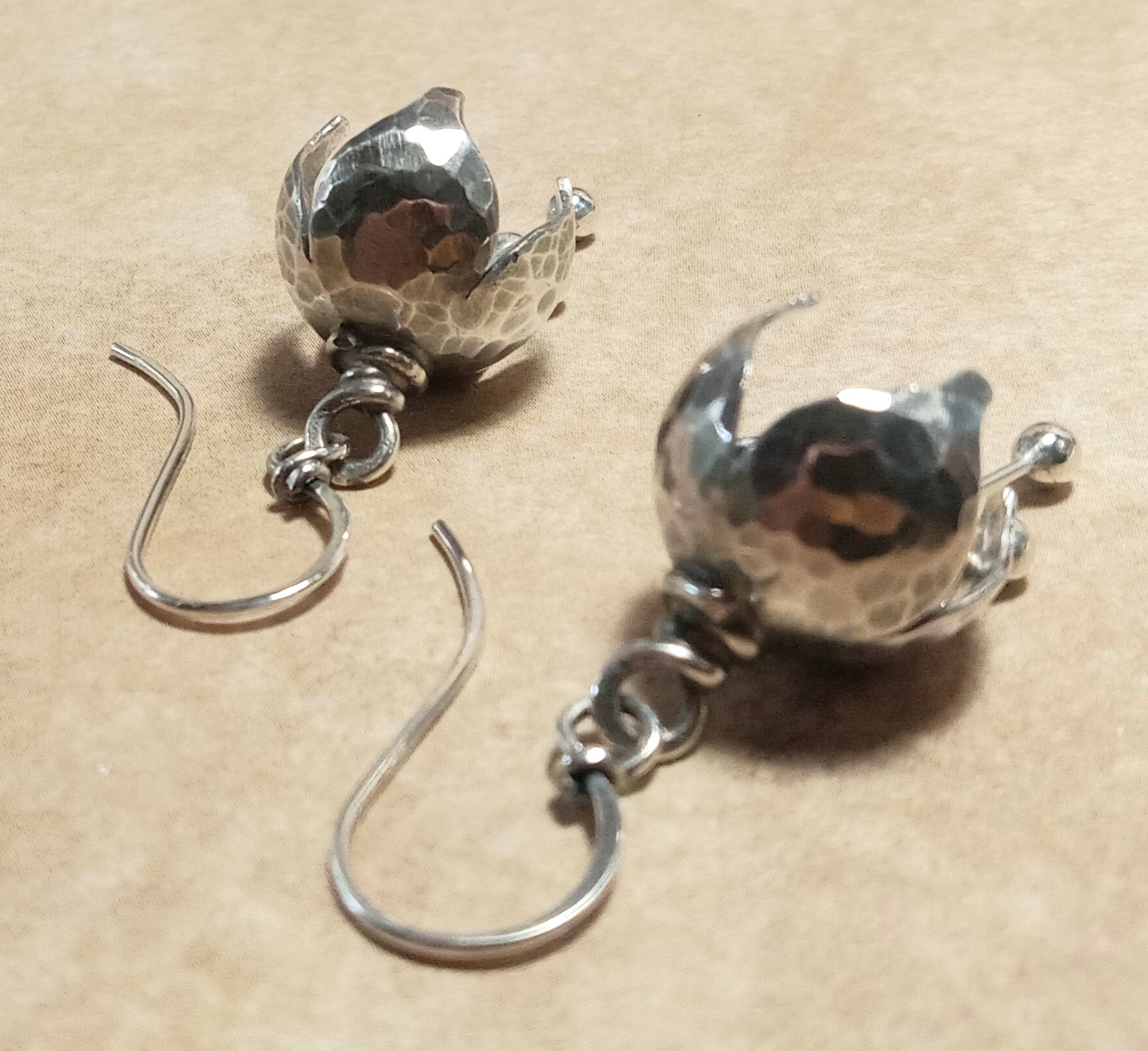 Pair of sterling silver bell shaped earrings on a beige background.
