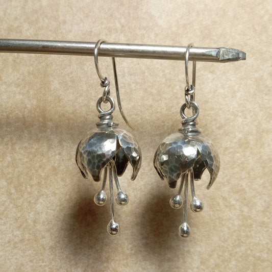Handcrafted petite bell flower earrings in Argentium sterling silver with hammered texture and three balled silver stamens that create a soft tinkling sound. Lightweight, oxidized, and polished for depth and shine. Suspended on stand.