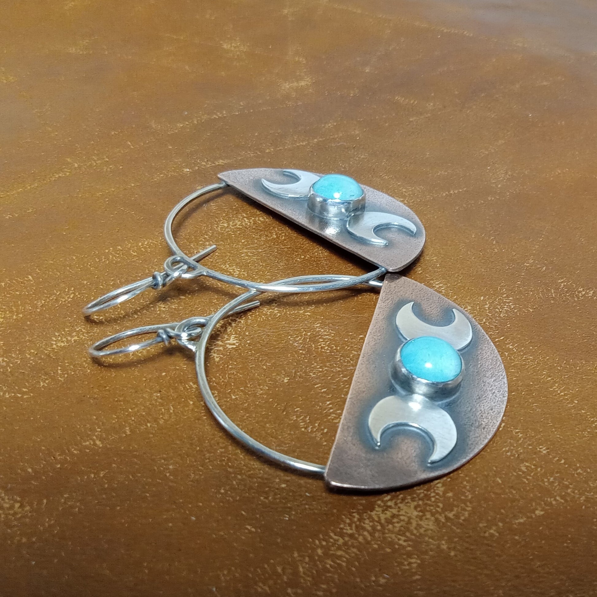 Side view of handcrafted copper and silver Triple Goddess earrings with blue amazonite stones against a brown background.