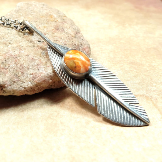 Handcrafted Argentium silver feather pendant with orange spiny oyster cabochon on rolo chain propped up on stone.