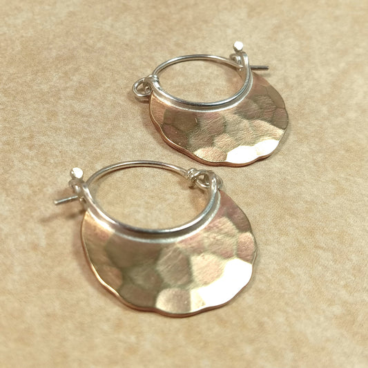 Close-up of bronze crescent hoop earrings with hammered texture and silver ear wires on neutral background