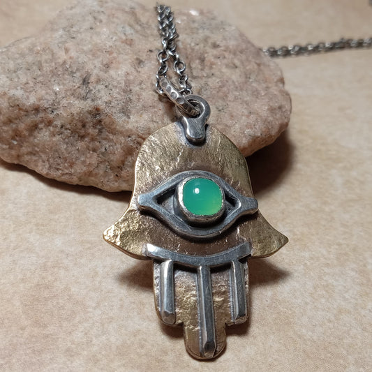 Bronze and Silver hamsa pendant with green gemstone on a stone background