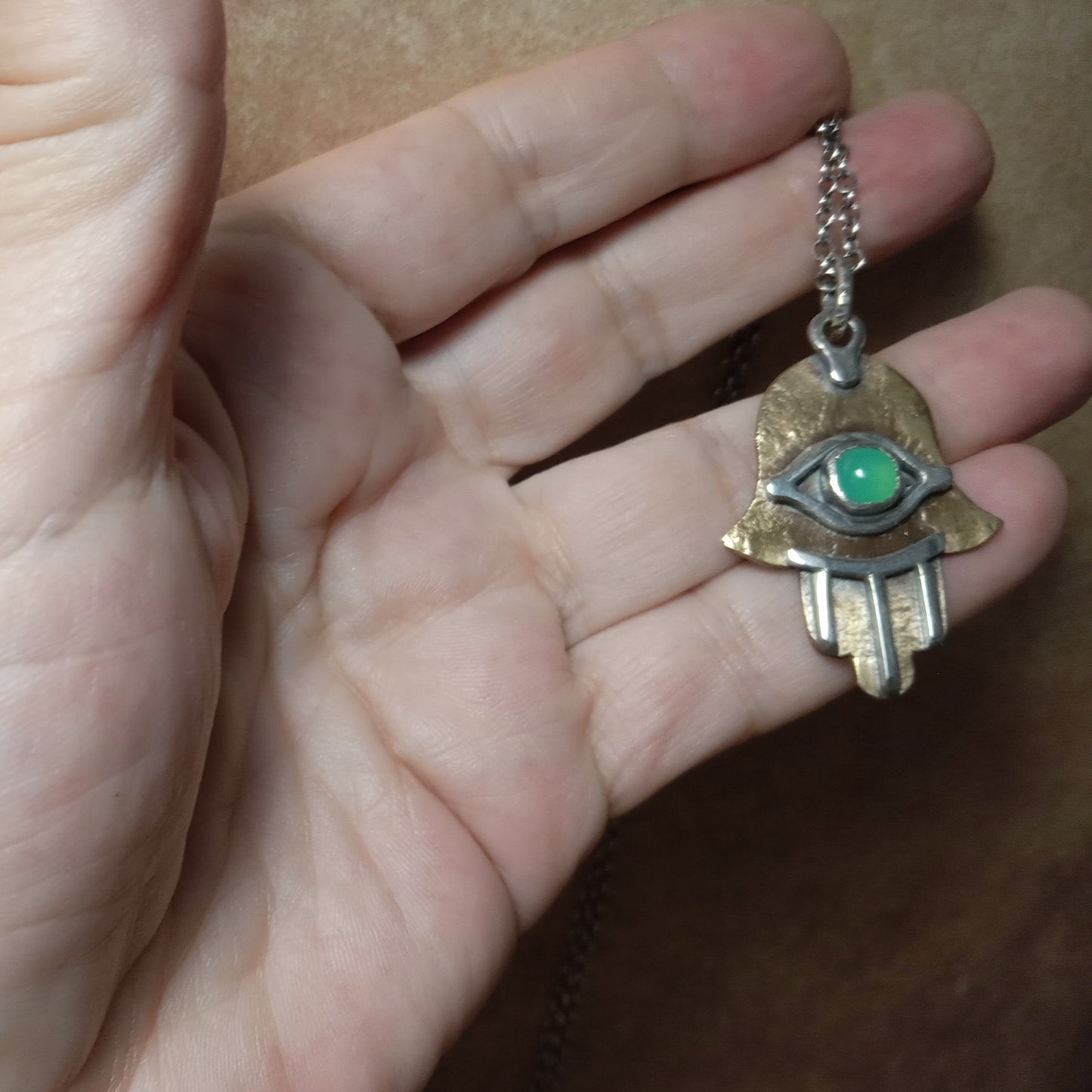 Hand holding a Hamsa necklace with a green eye.