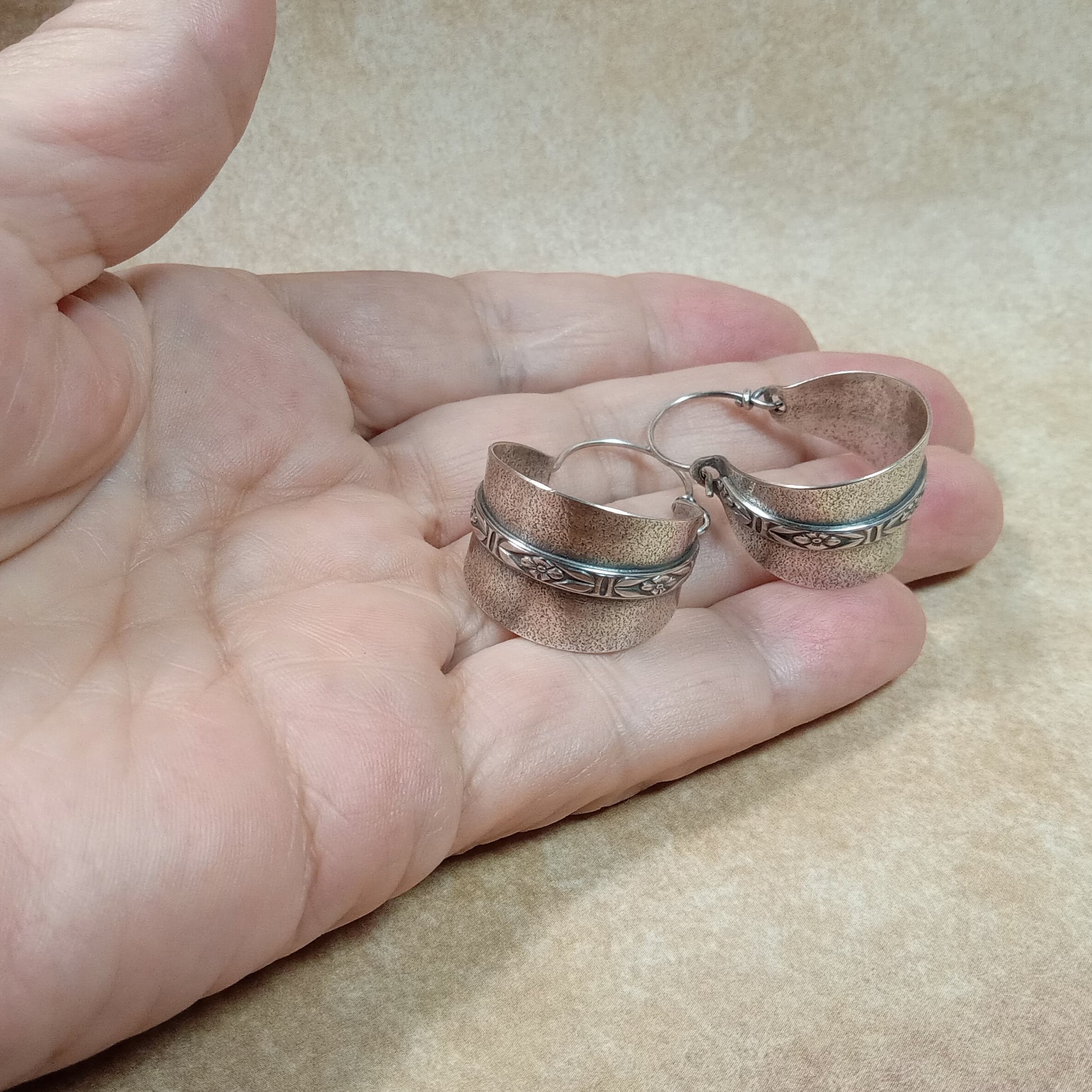 Pair of argentium silver hoop earrings by Mocahete held in hand on a beige background.