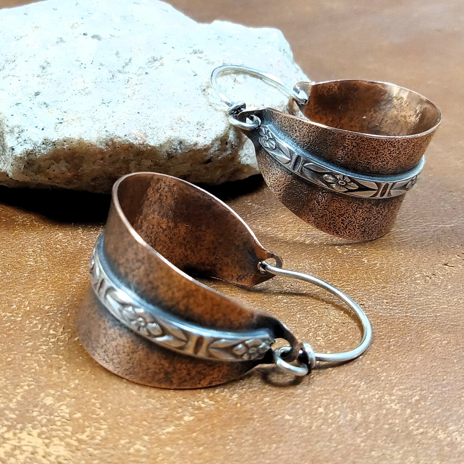 Oxidized copper and sterling silver hoop earrings, handmade jewelry on brown background with stone.