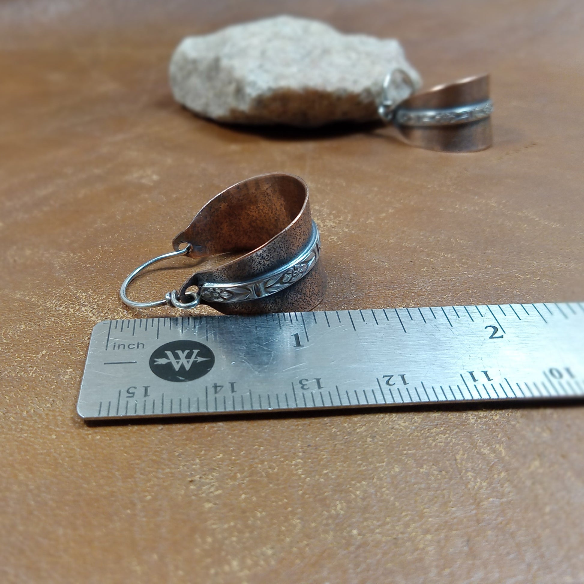 Lightweight artisan copper and silver hoops by Mocahete against ruler on brown background with stone .