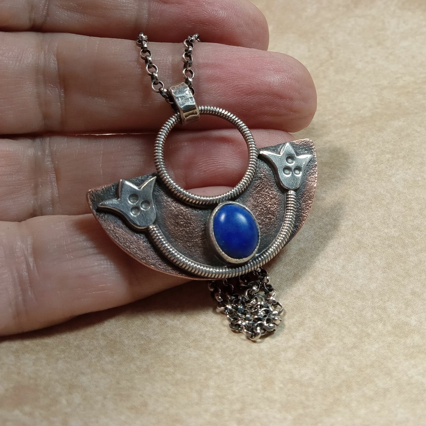 Photo of hand holding handcrafted copper and silver lotus pendant with lapis stone.