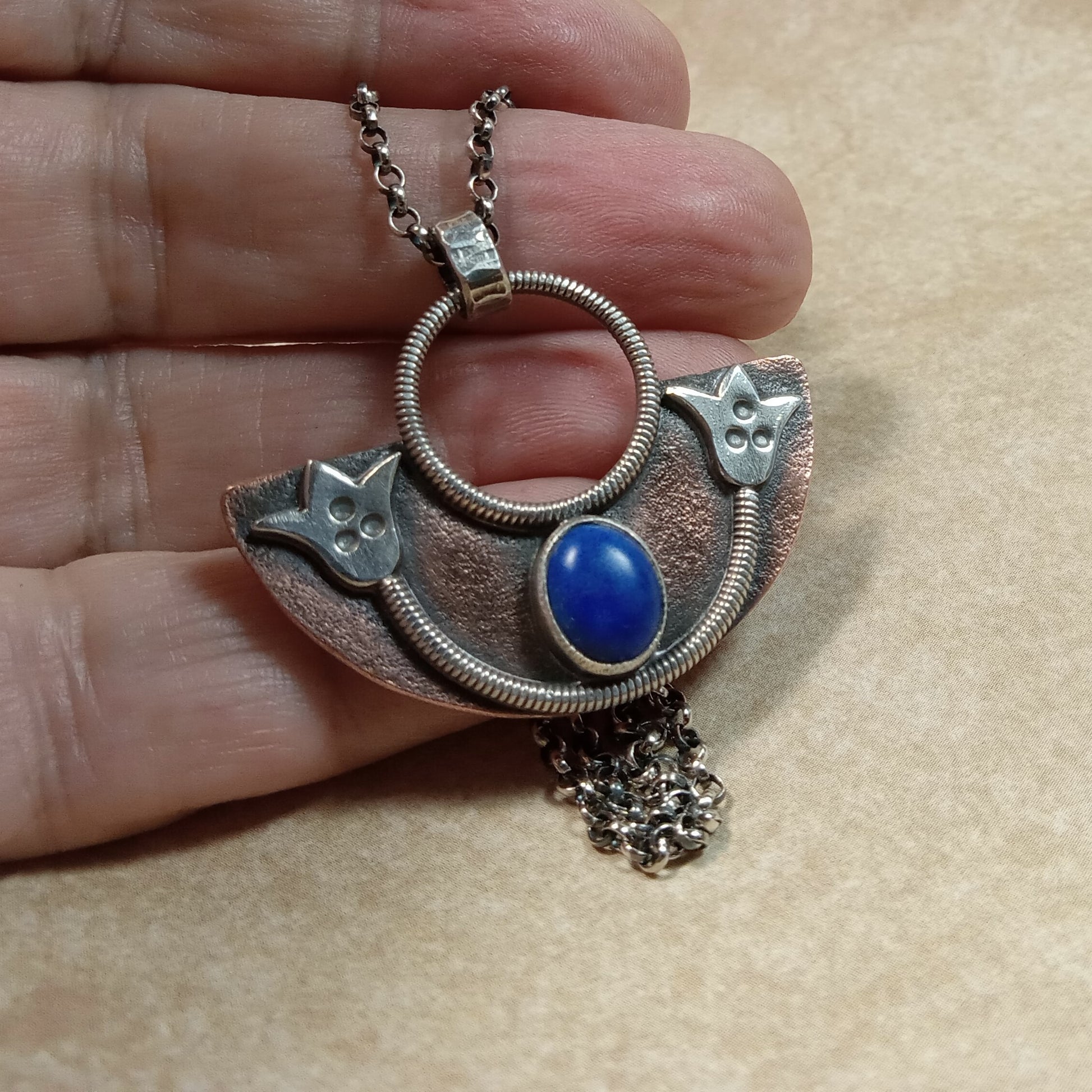 Photo of hand holding handcrafted copper and silver lotus pendant with lapis stone.