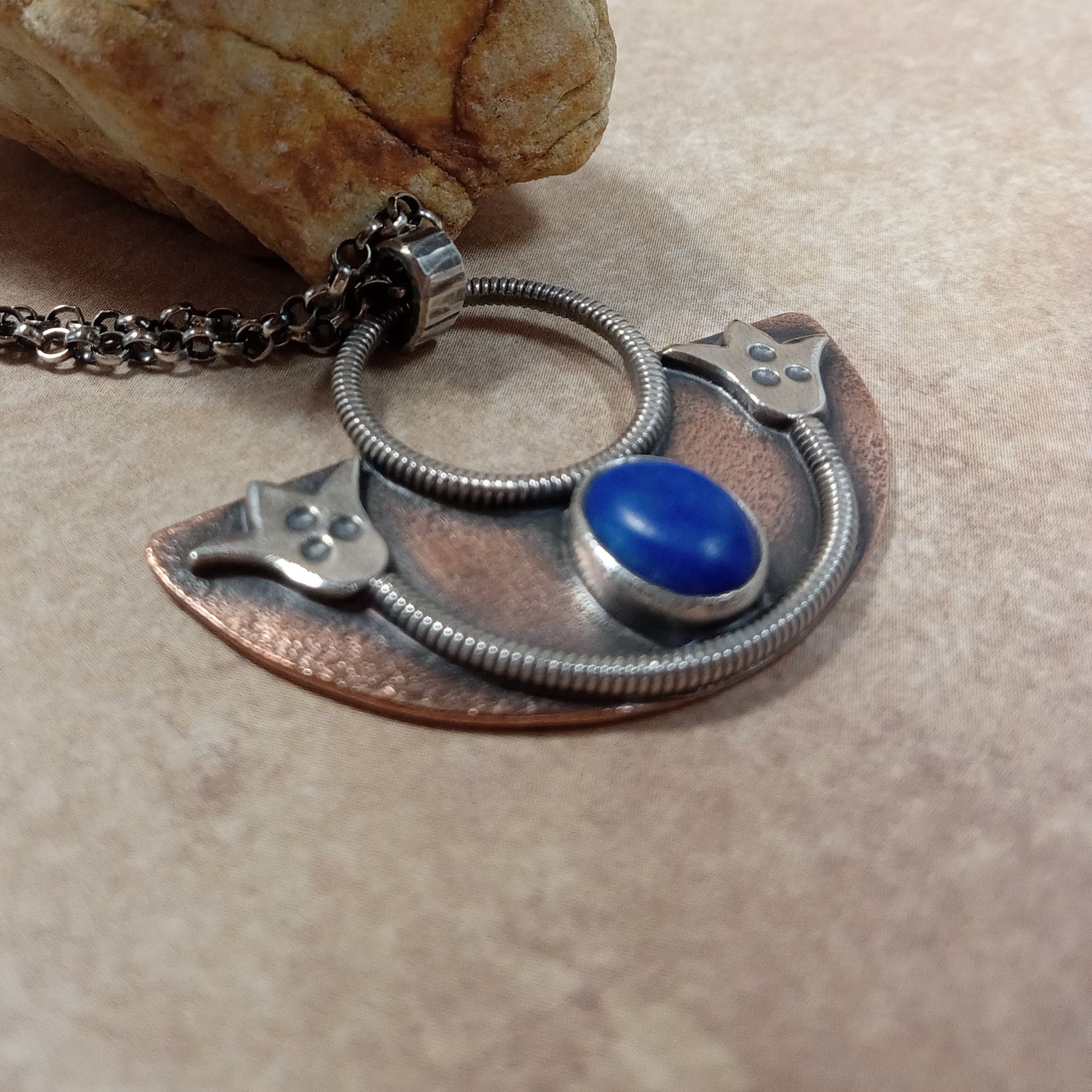 Mixed metal lotus pendant in copper and silver with lapis lazui stone by Mocahete. Beige background with stone prop.