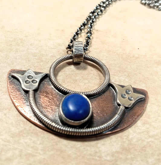 Handcrafted lotus pendant necklace in copper and Argentium silver with lapis lazuli cabochon on beige background.