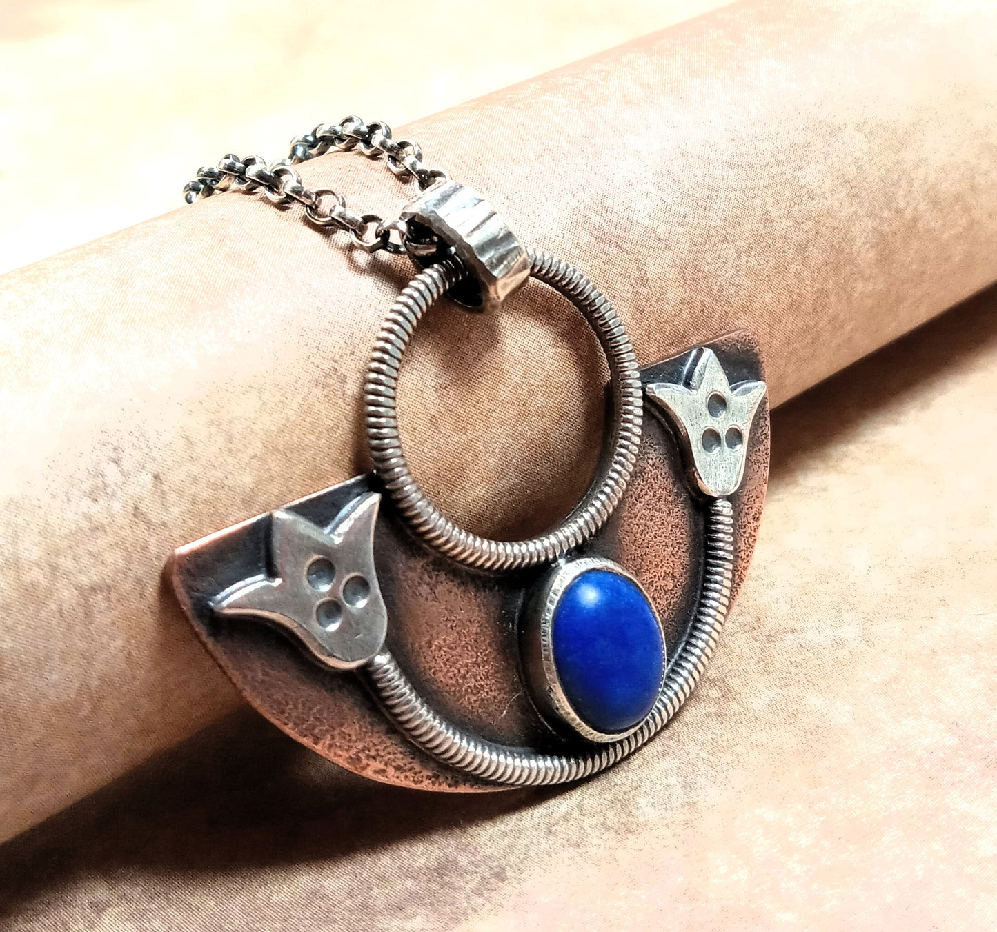Close up of mixed metal and lapis lotus pendant against beige background.