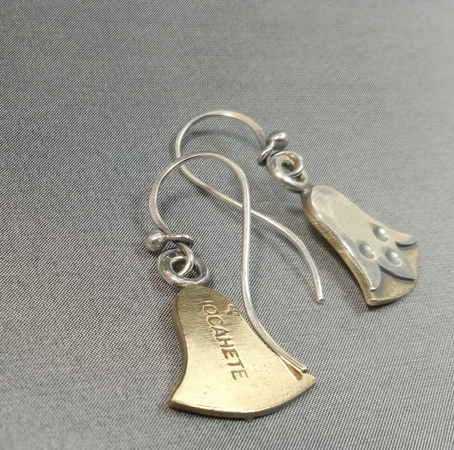 Reverse side of lotus flower earrings show Mocahete makers mark on grey background