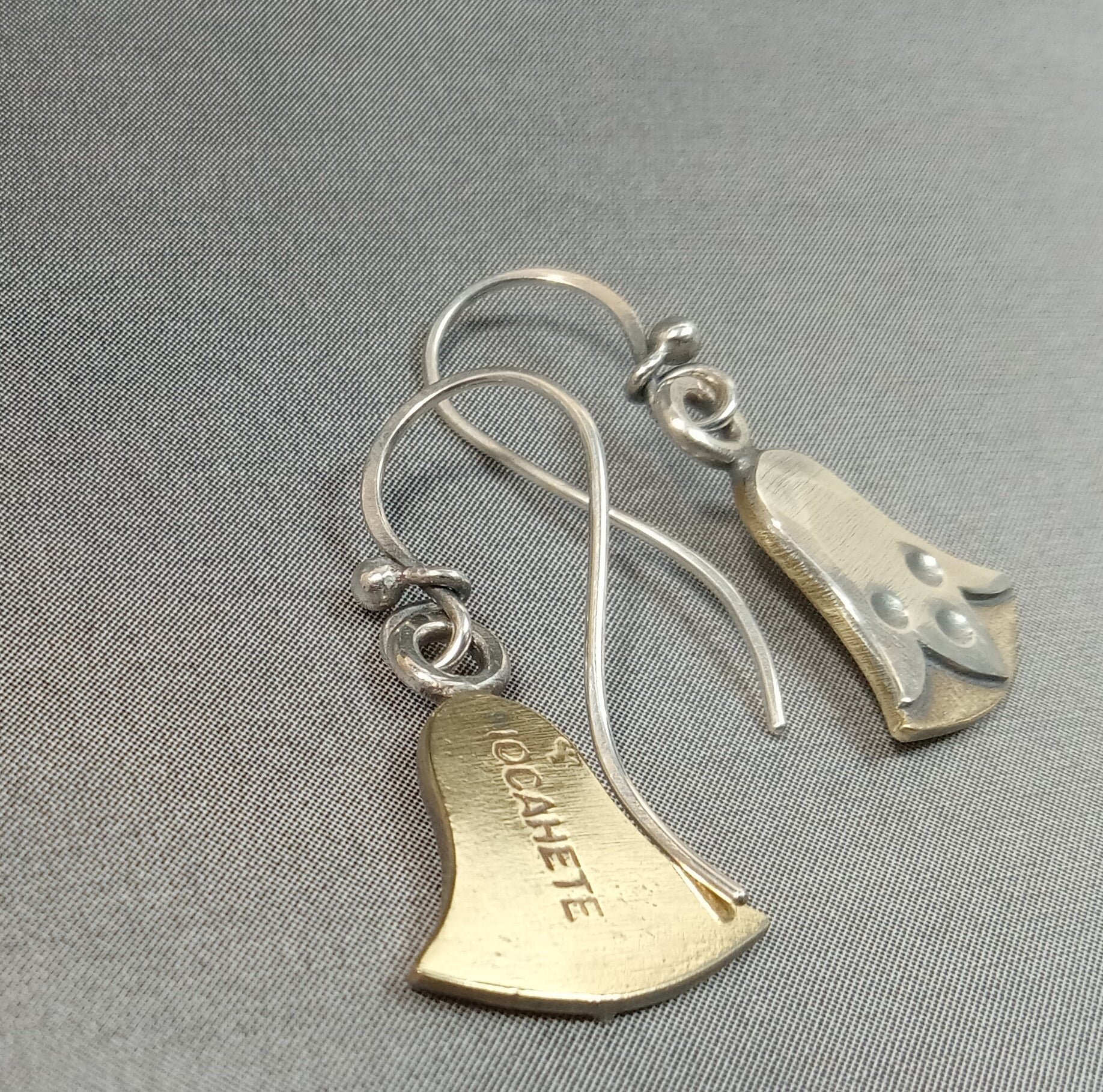 Reverse side of lotus flower earrings show Mocahete makers mark on grey background