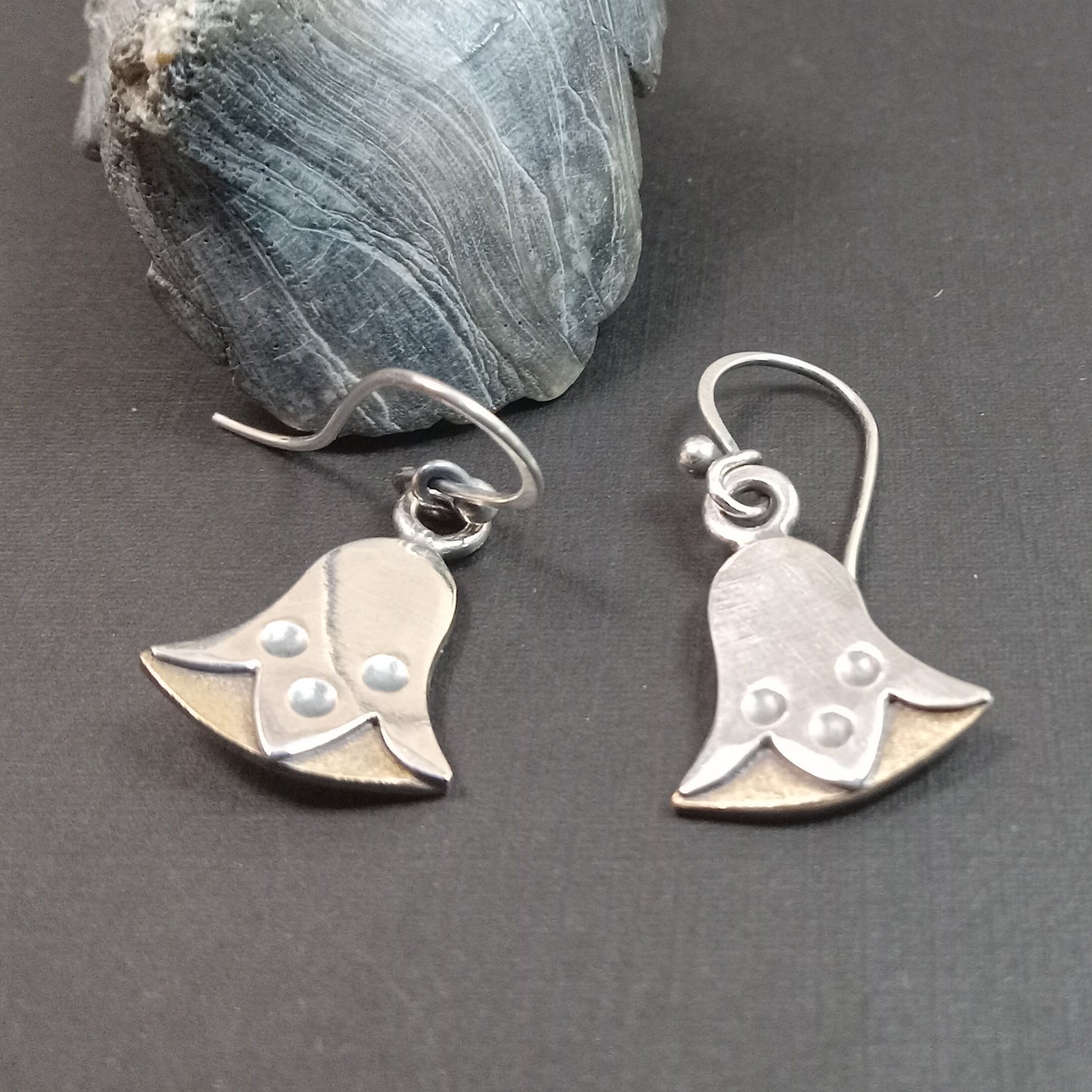 Silver and bronze egyptian lotus shaped earrings on a gray surface with a stone in the background
