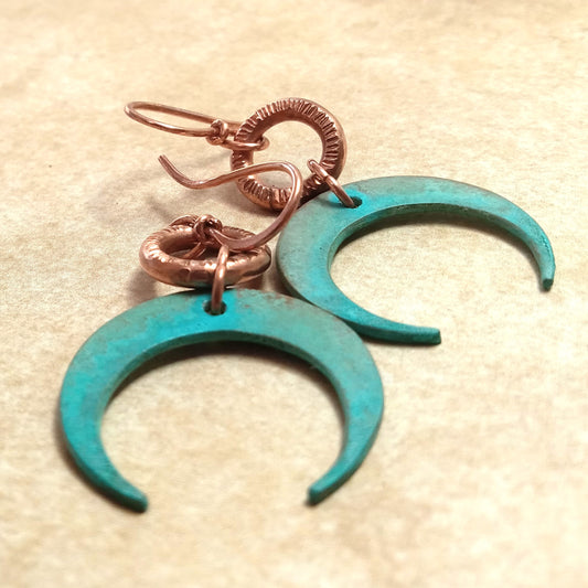 Blue patina crescent moon earrings with copper hooks on a beige background