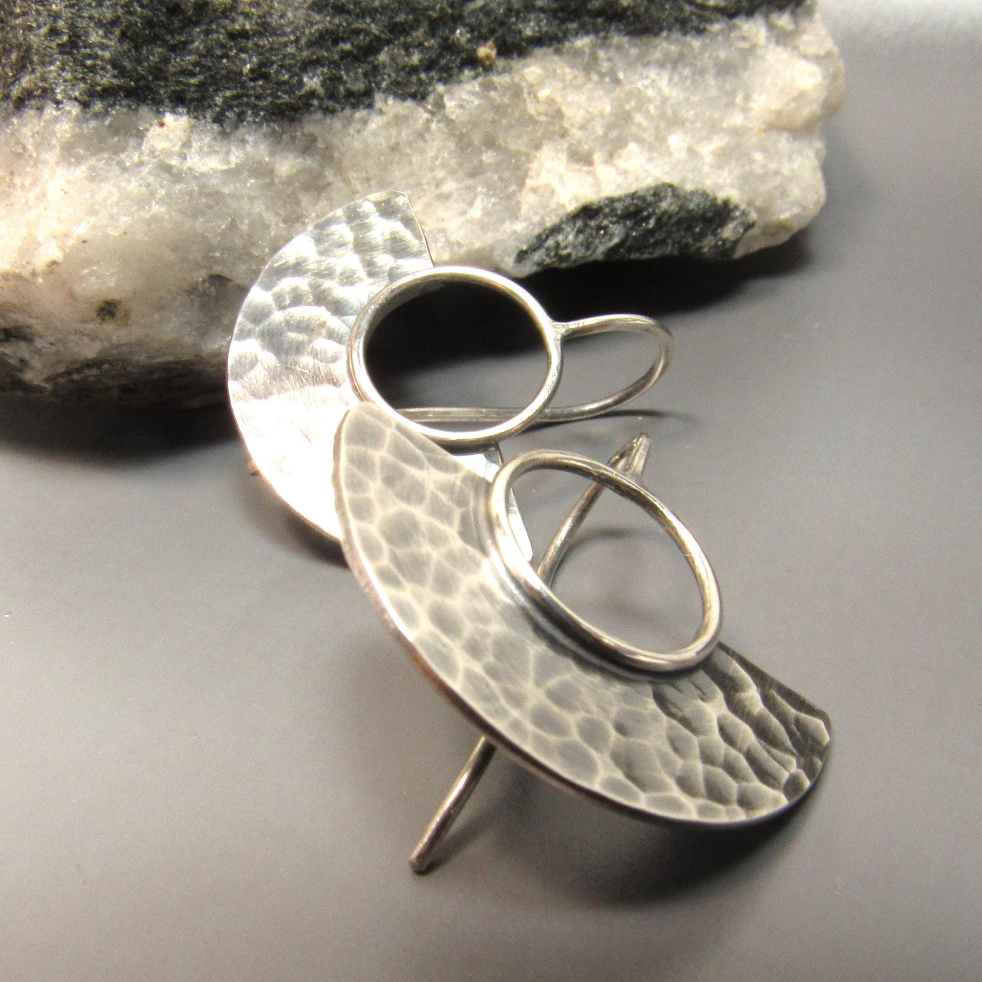 Fan shape argentium silver earrings with a textured design on a stone background.