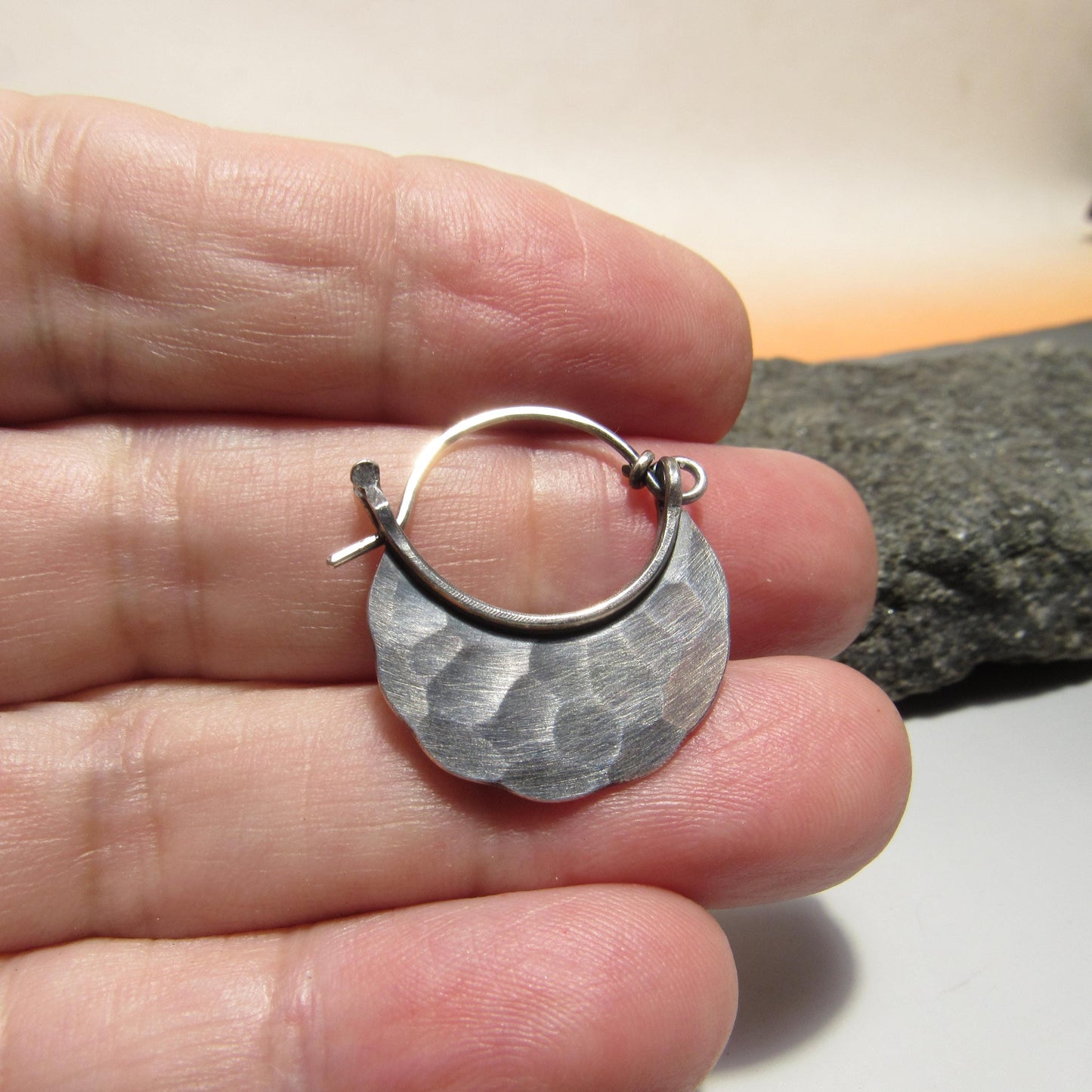 Silver hoop earring held between fingers with a rock background