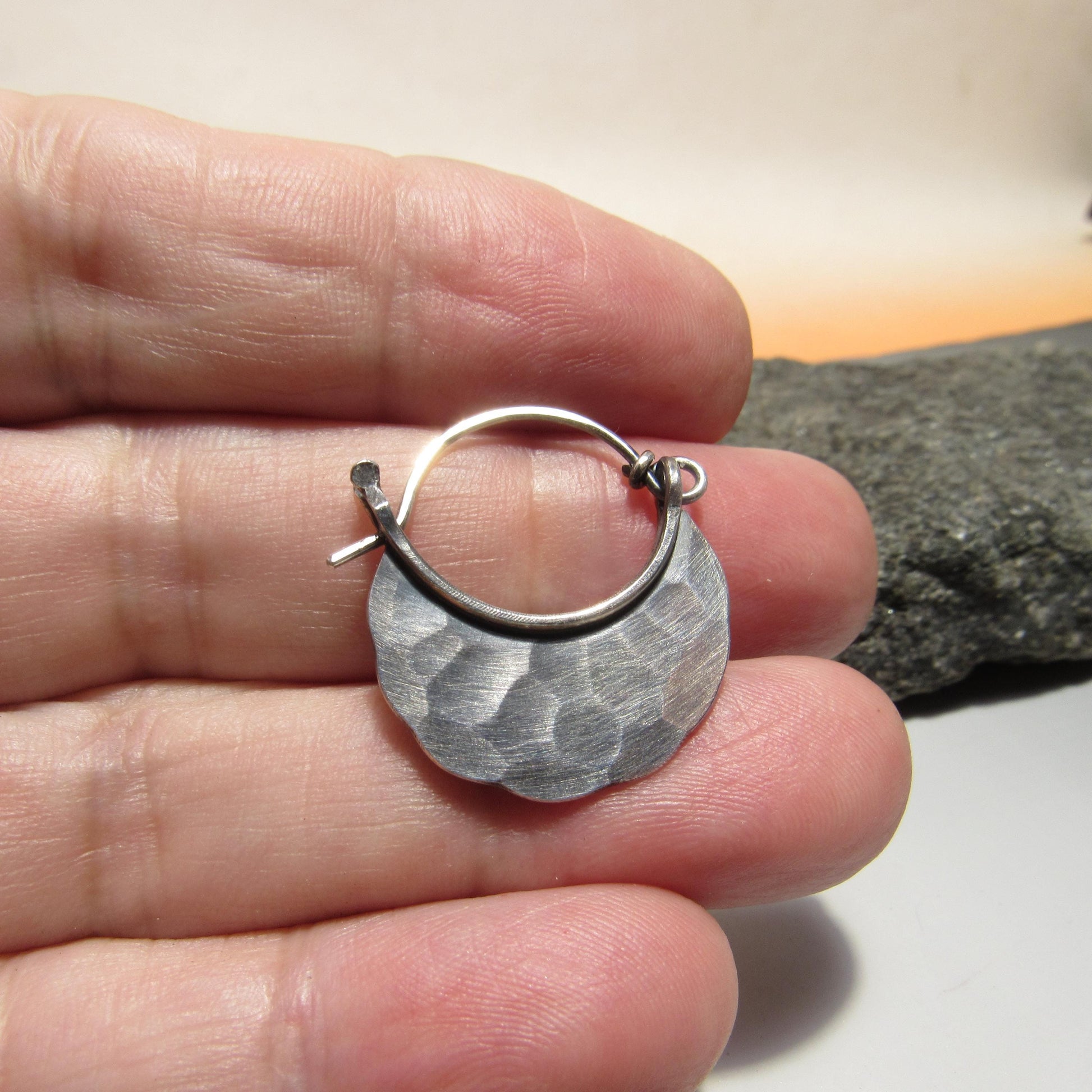 Silver hoop earring held between fingers with a rock background