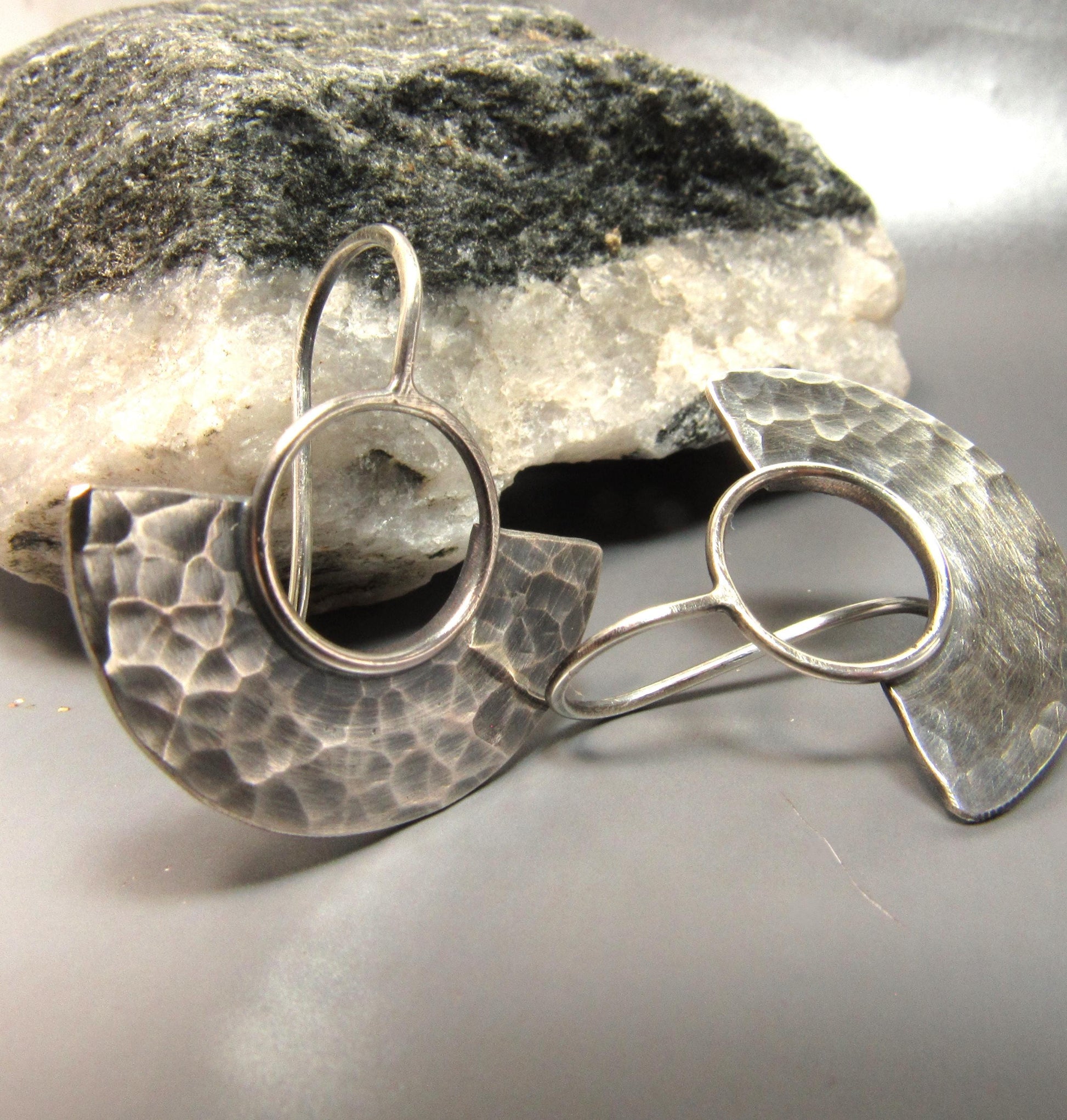 Pair of hammered half circle  silver earrings on a stone surface.