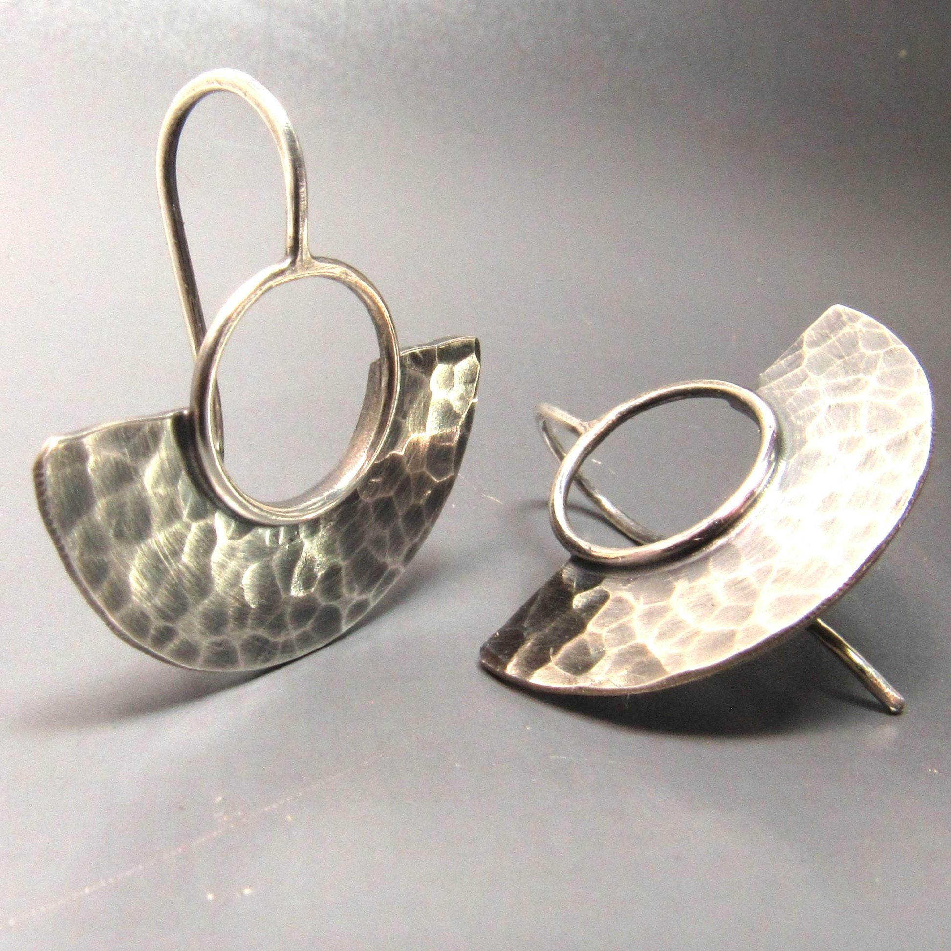 Pair of silver earrings with hammered finish on a gray background.