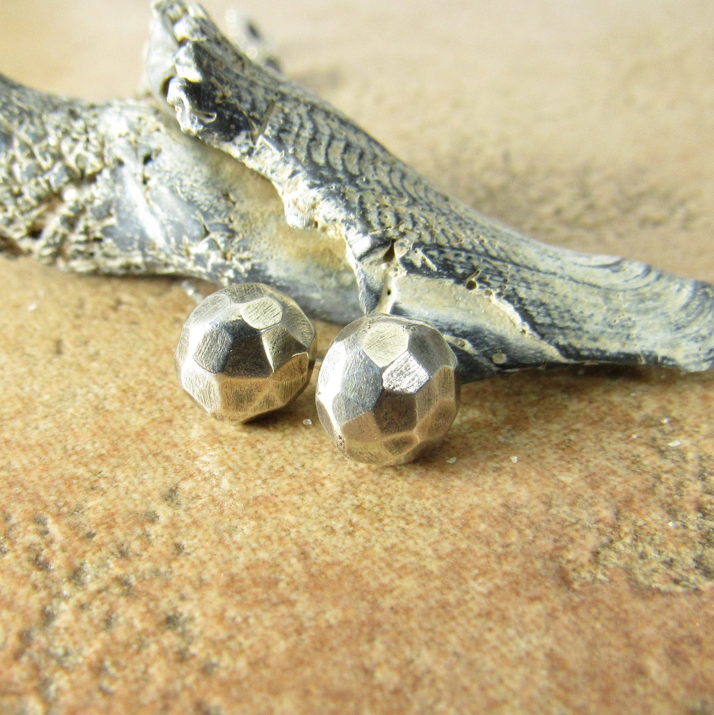 Faceted silver nugget stud earrings with sea shell and textured beige background.