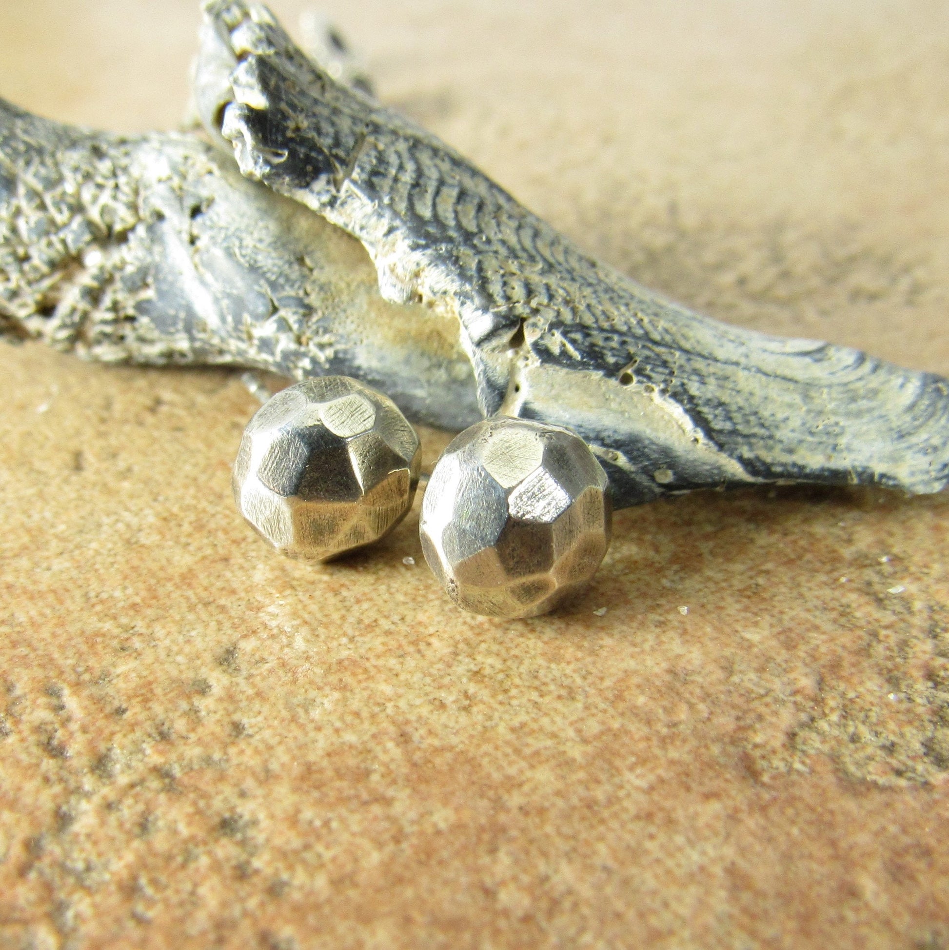 Faceted silver nugget stud earrings with sea shell and textured beige background.