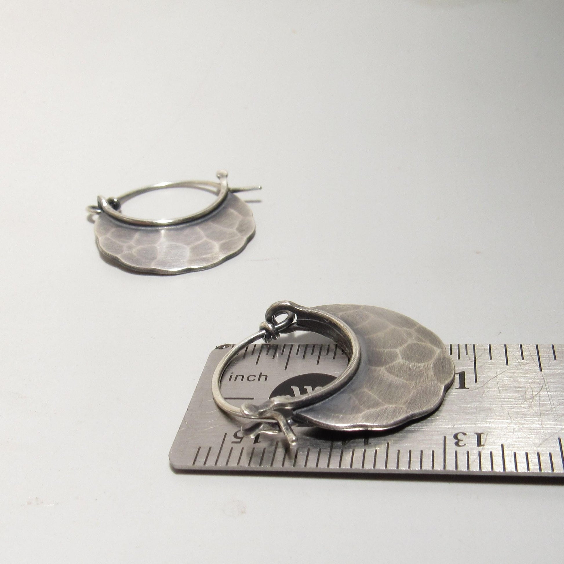 Silver hoop earrings with textured design on a white background, shown next to a ruler for size reference.