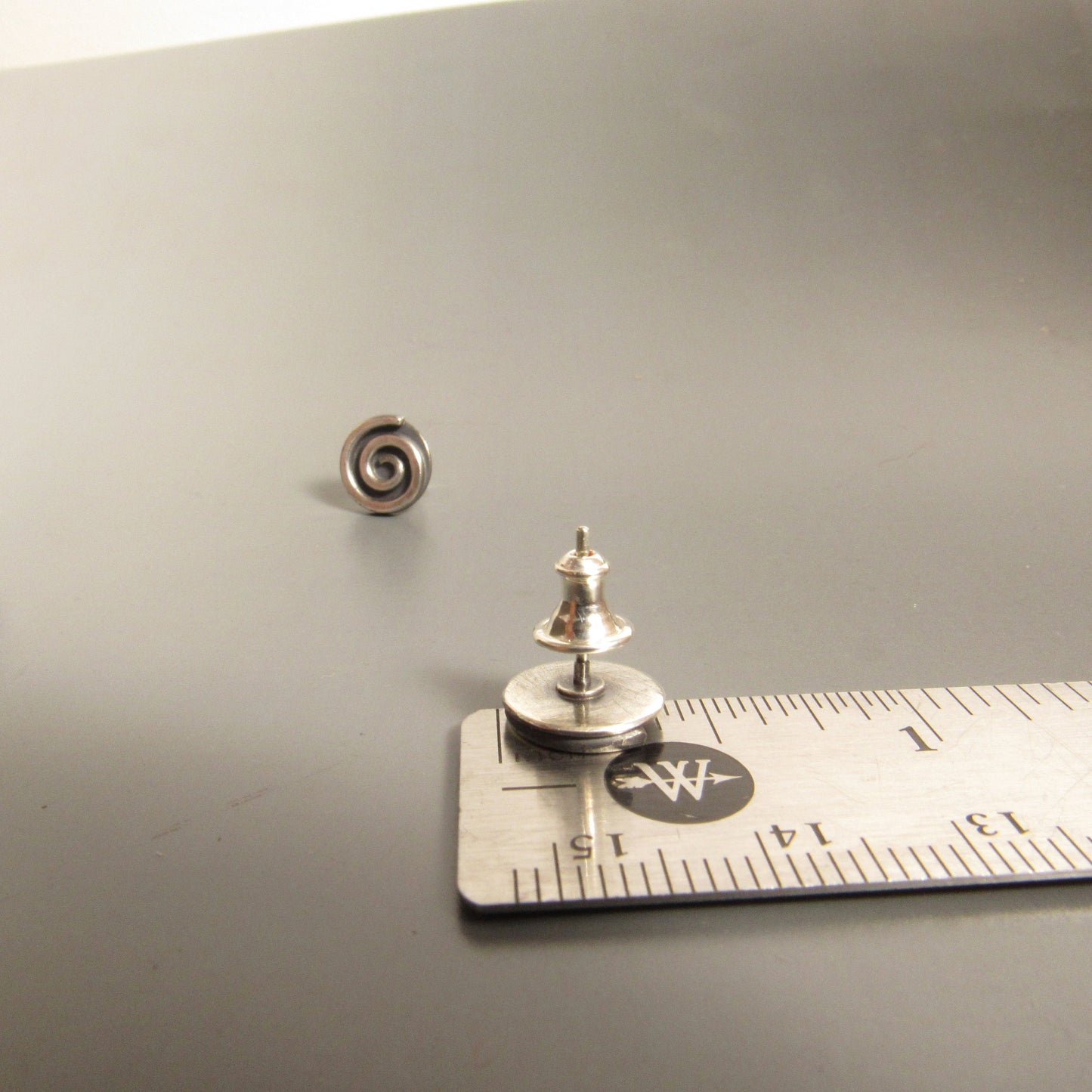 SS spiral stud earrings on a gray surface with a ruler for scale.